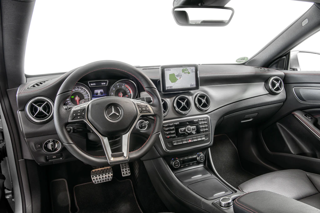 Innenraum eines modernen Autos mit Lenkrad, Tachometer und Display auf der Mittelkonsole. Schwarze Sitze und silberne Akzente.