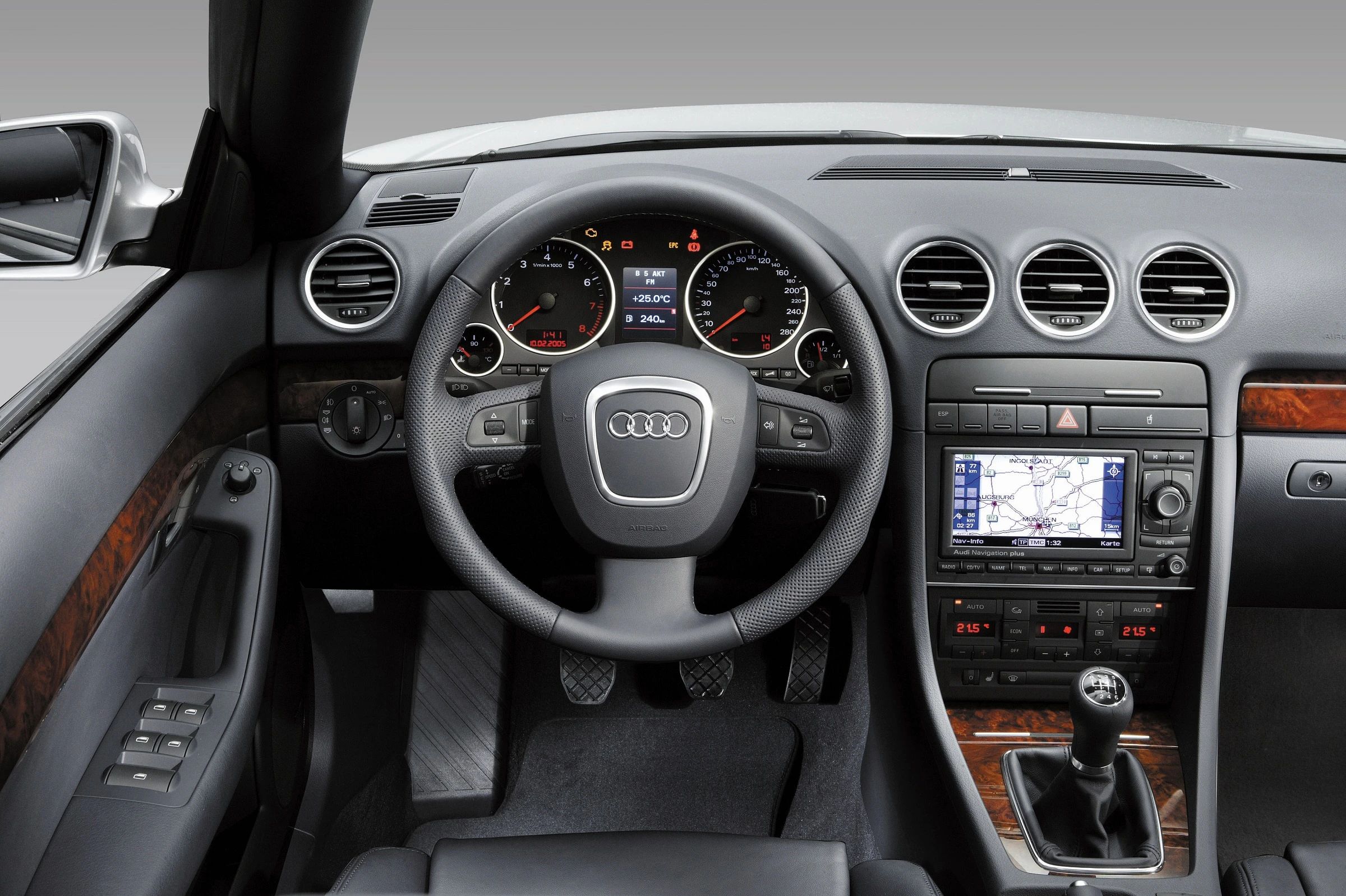 Innenraum eines Audis mit Lederlenkrad, Rundinstrumenten, Holzverkleidung, manuellem Getriebe und Navigationssystem auf der Mittelkonsole.