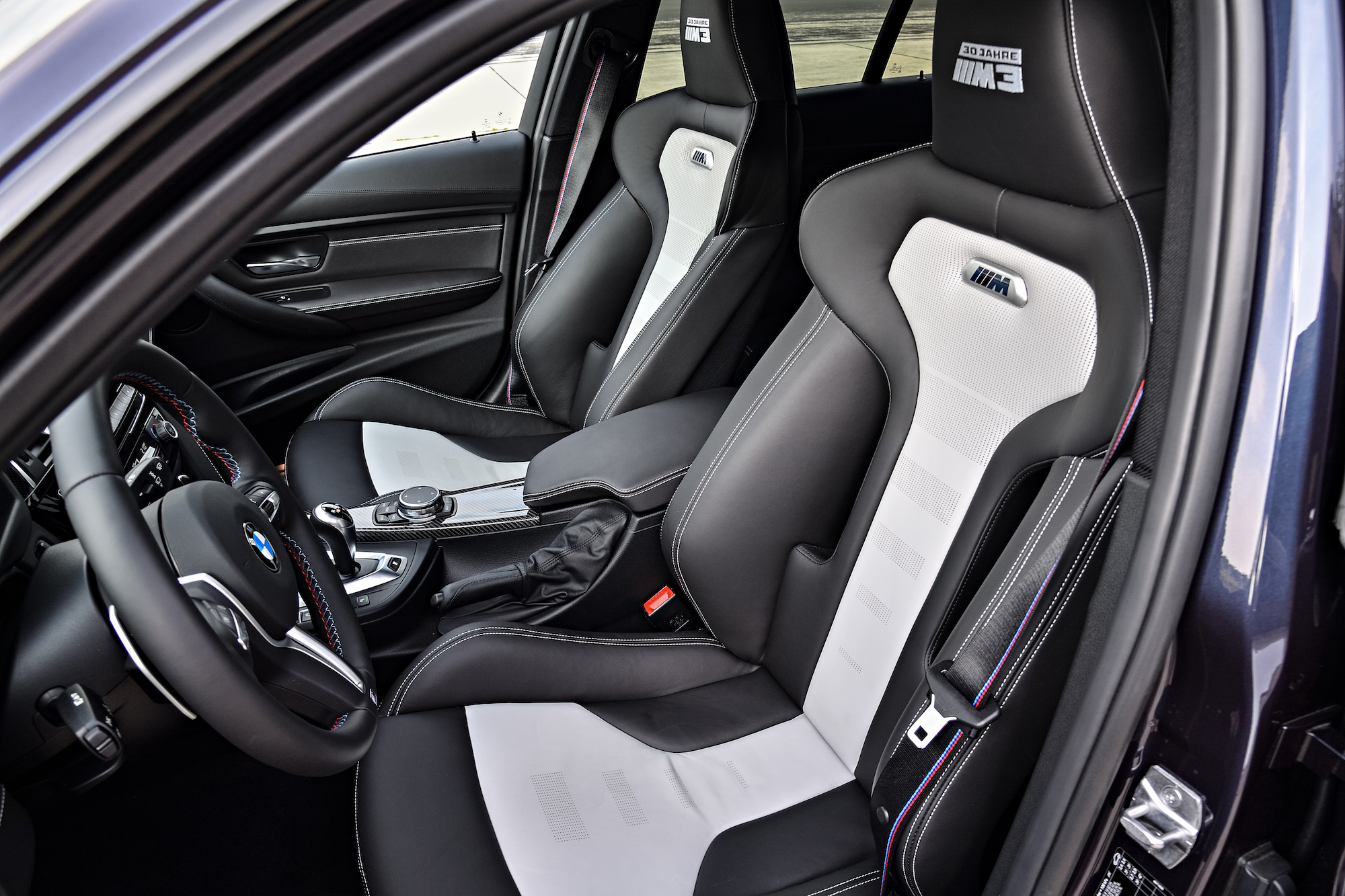 Innenraum eines Autos mit schwarzen Sportsitzen, weißen Akzenten und einem zentralen Armaturenbrett mit Steuerungselementen.