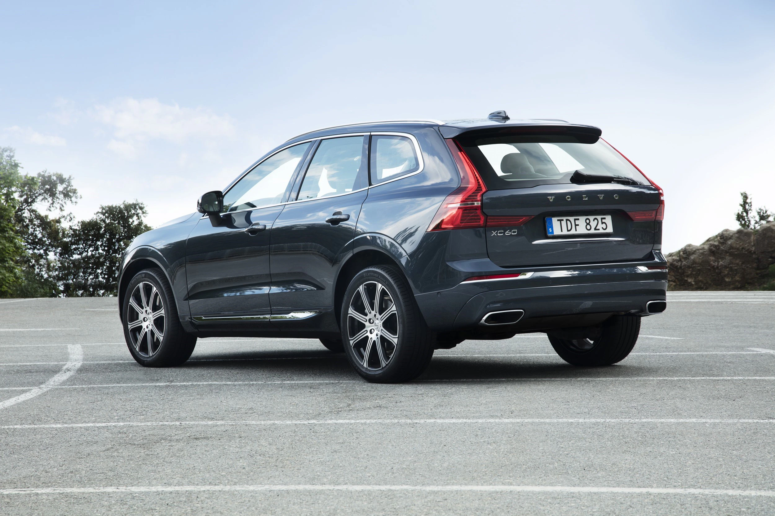 Ein dunkelgrauer Volvo XC60 steht auf einem Parkplatz, umgeben von Bäumen im Hintergrund. Die Perspektive zeigt die Rückansicht des Autos.