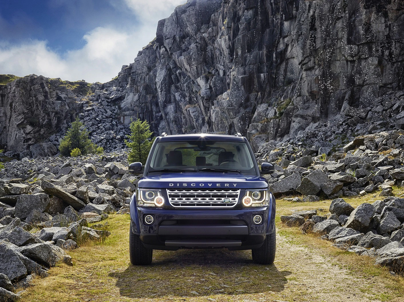 Land Rover Discovery auf steinigem Weg in bergiger Landschaft bei bewölktem Himmel, von vorne gesehen.