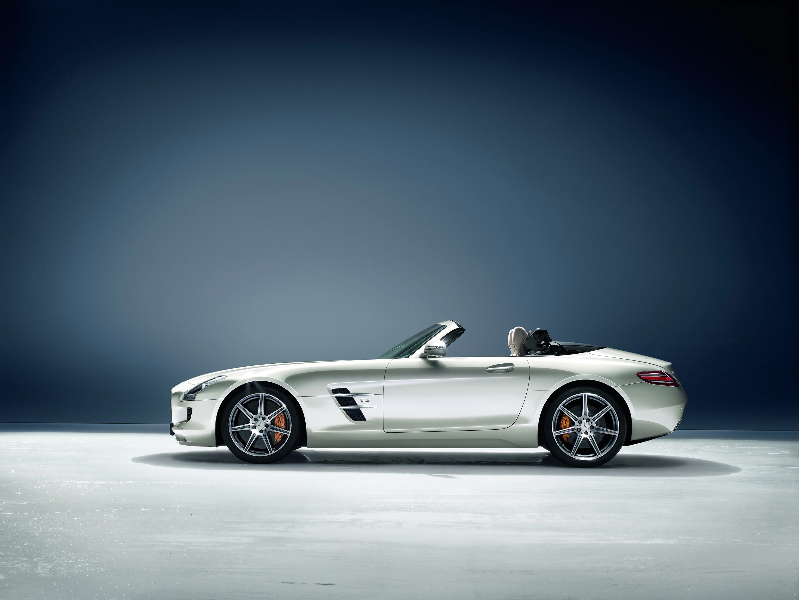 Silbernes Cabrio in seitlicher Ansicht vor blauem Hintergrund. Oben offen, sportliches Design, rote Bremssättel, modern und elegant.