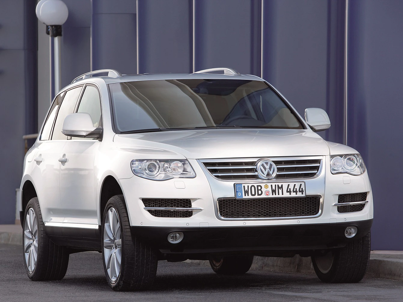 Weißer SUV der Marke Volkswagen Touareg, Frontansicht, geparkt vor einer modernen, blauen Wand.