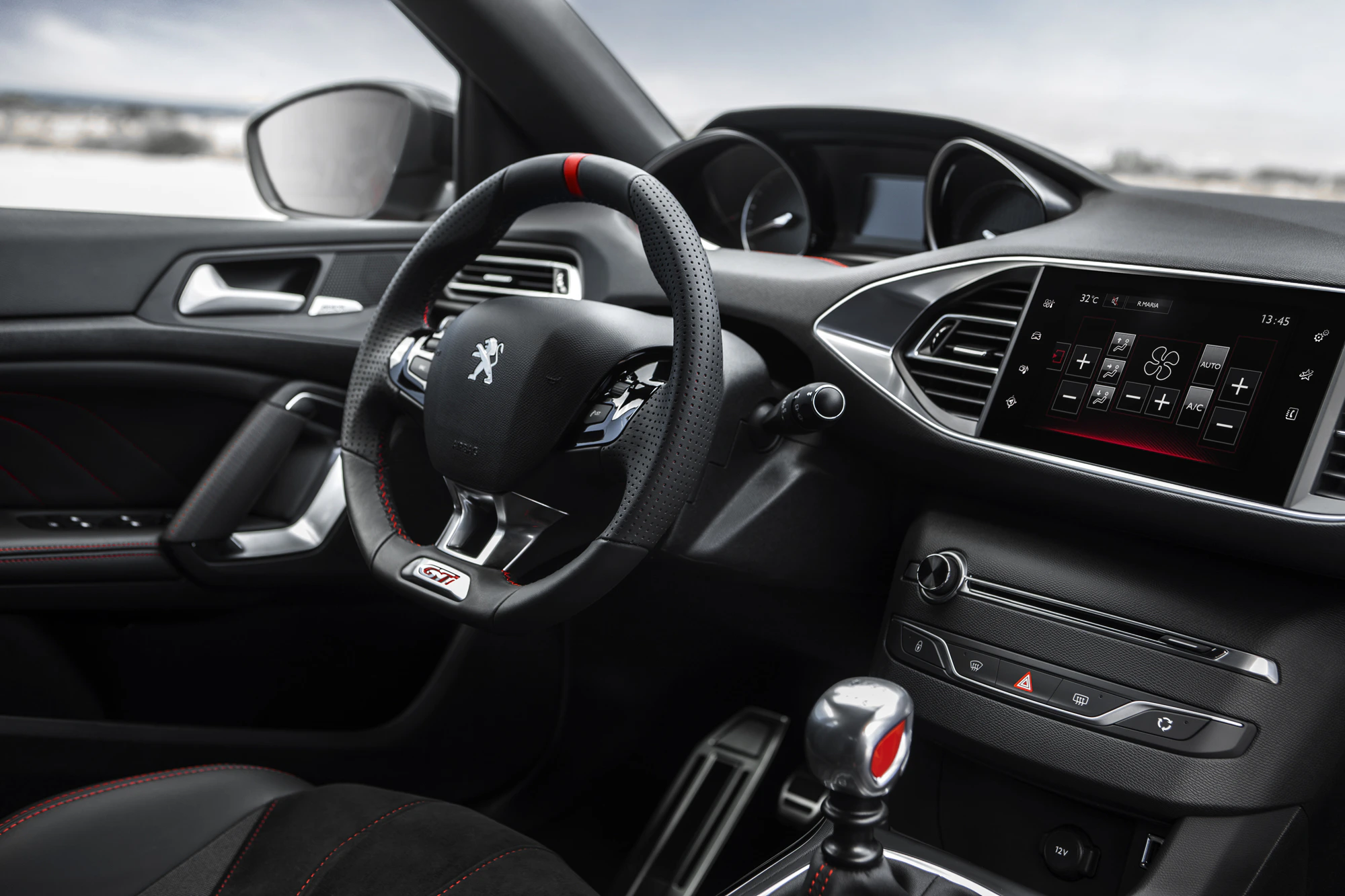Innenraum eines modernen Autos, mit einem Peugeot-Logo auf dem Lenkrad, digitalem Display und Details in Schwarz und Rot.