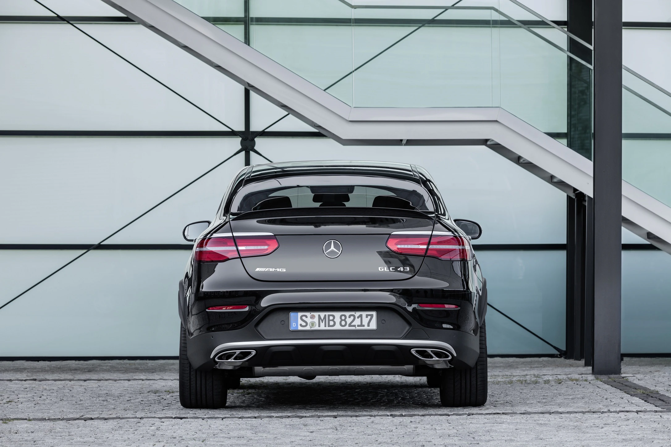 Rückansicht eines schwarzen Mercedes-Benz GLC 43 vor einer modernen Glasfassade mit Treppe im Hintergrund.