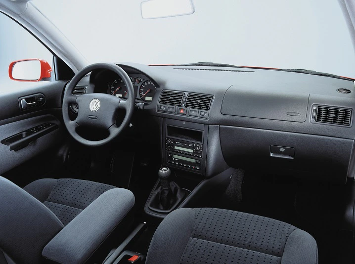 Innenraum eines Autos mit schwarzem Interieur, Lenkrad mit VW-Logo, Schaltknüppel und Armaturenbrett mit Klimaanlage und Radio.