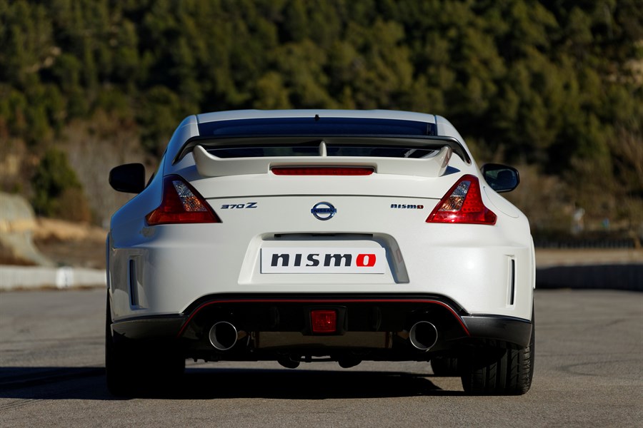 Weißer Sportwagen Nissan 370Z Nismo von hinten auf einer Straße, hinten zweifacher Auspuff, im Hintergrund bewaldete Hügel.
