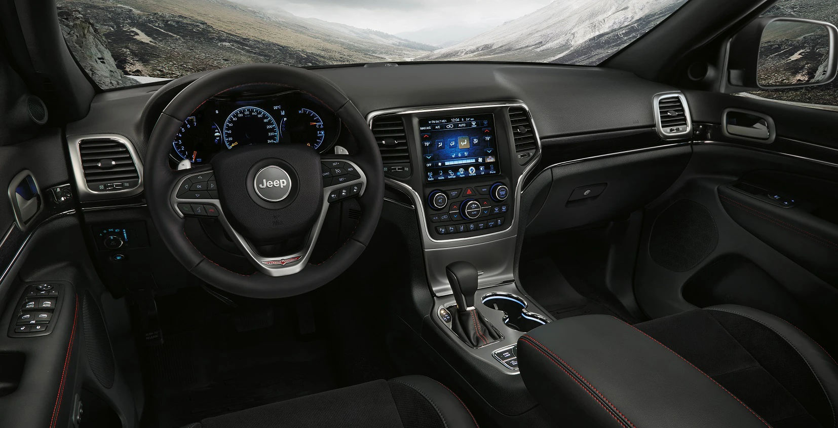 Innenraum eines Jeep mit modernem Armaturenbrett, großem Touchscreen-Display und Ledersitzen. Schnee bedeckte Landschaft sichtbar durch die Fenster.