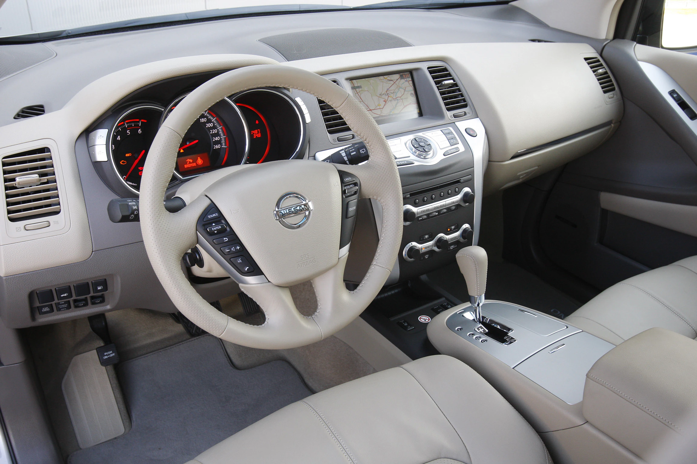 Innenraum eines Autos mit beigem Leder; zeigt Lenkrad, Automatikgetriebe, Armaturenbrett mit Tacho und Navigationssystem.
