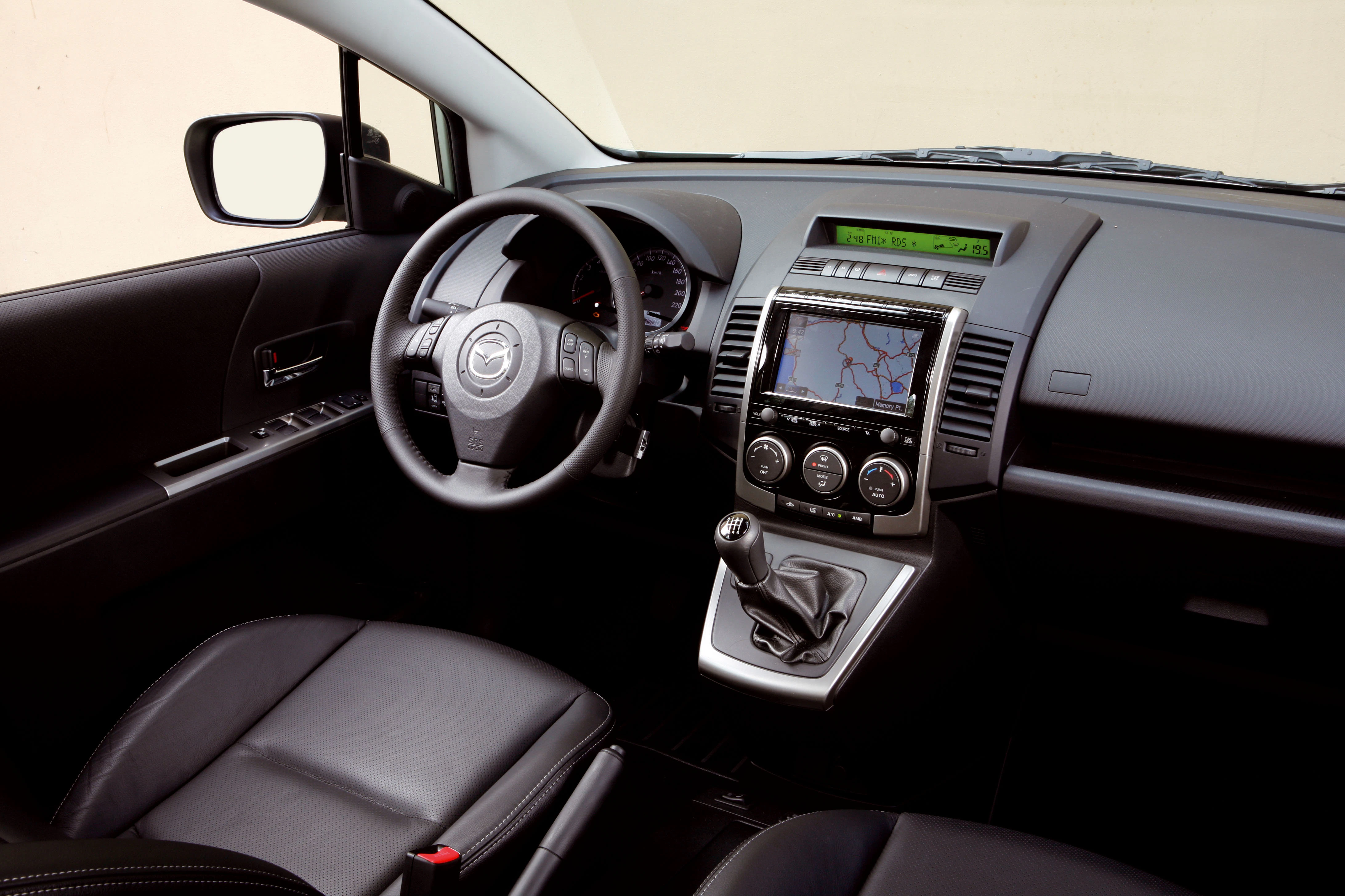 Innenraum eines Autos mit Lederpolstern, manuellem Schalthebel, Lenkrad, Tachometer und einem Navigationssystem auf der Mittelkonsole.