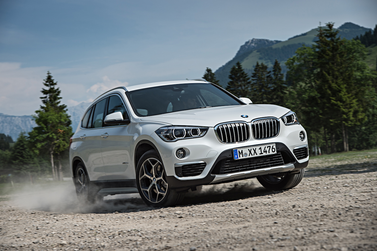 Weißer BMW SUV fährt auf einer staubigen Straße in einer bergigen Landschaft mit Bäumen im Hintergrund.