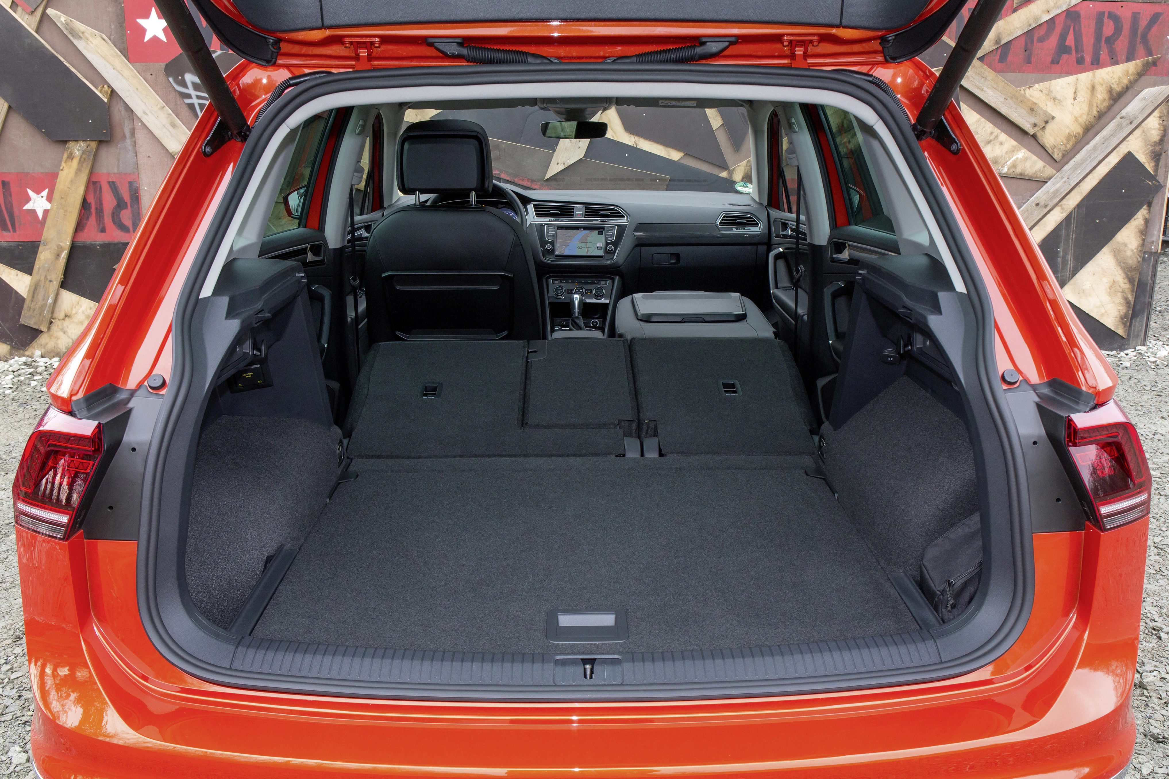 Kofferraum eines orangefarbenen SUVs mit umgeklappten Rücksitzen, zeigt großen Laderaum vor einem Hintergrund aus Holzbrettern und Sternen.