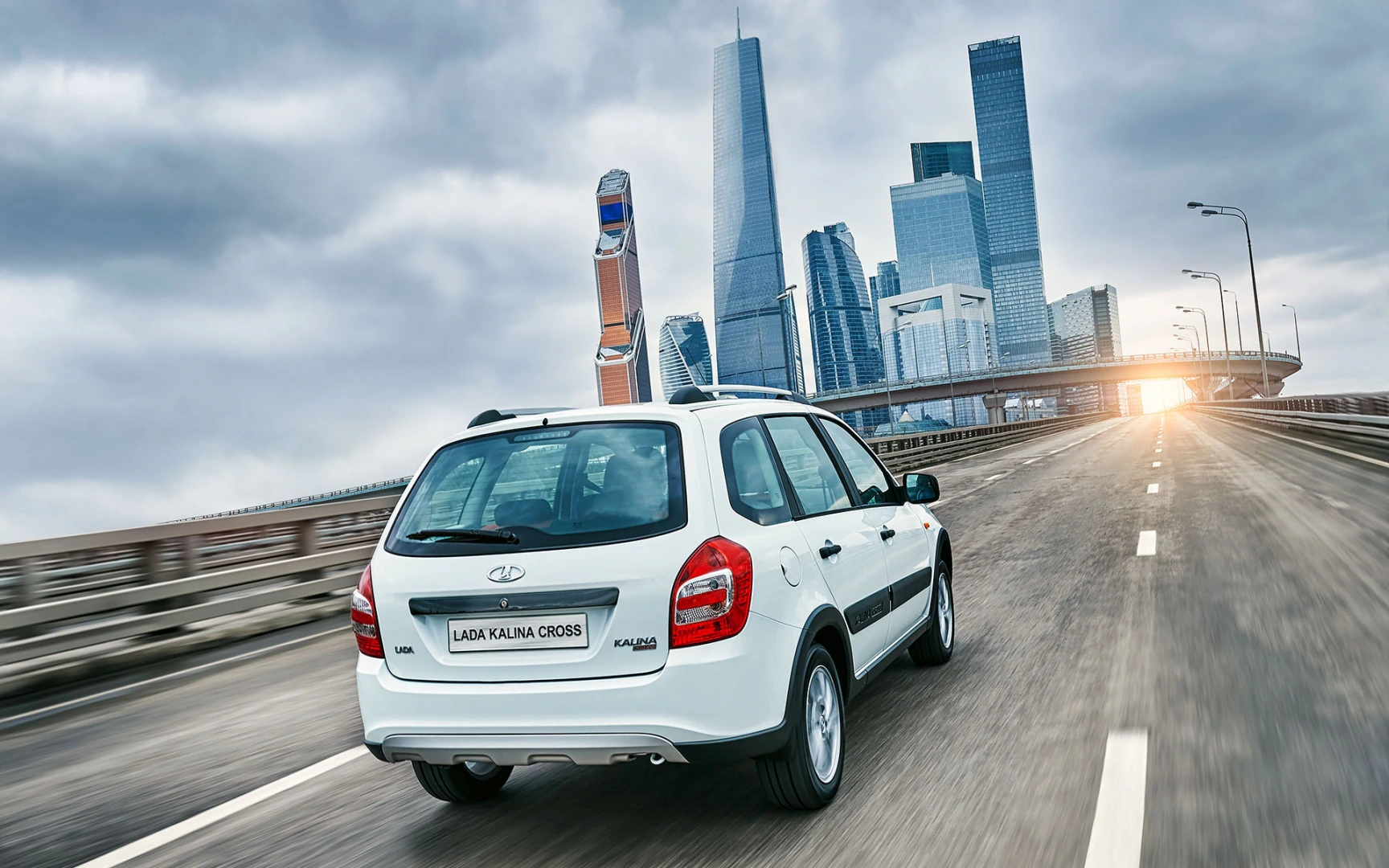 Ein weißer Lada Kalina Cross fährt auf einer leeren Stadtautobahn, im Hintergrund moderne Hochhäuser und ein Abendhimmel.