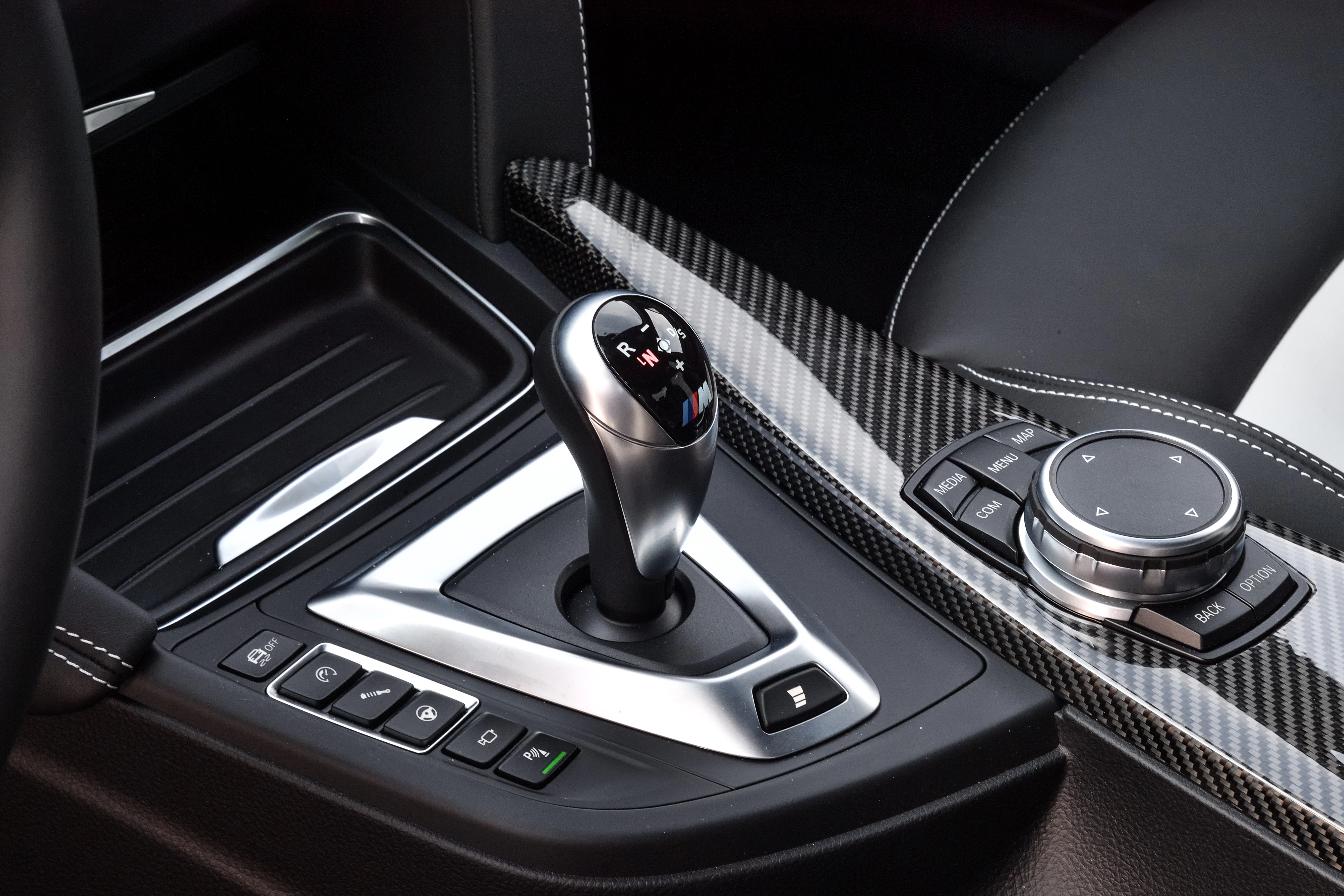 Nahaufnahme eines modernen Automatikgetriebes in einem Auto mit Kohlefaser-Details und Bedienelementen auf der Mittelkonsole.