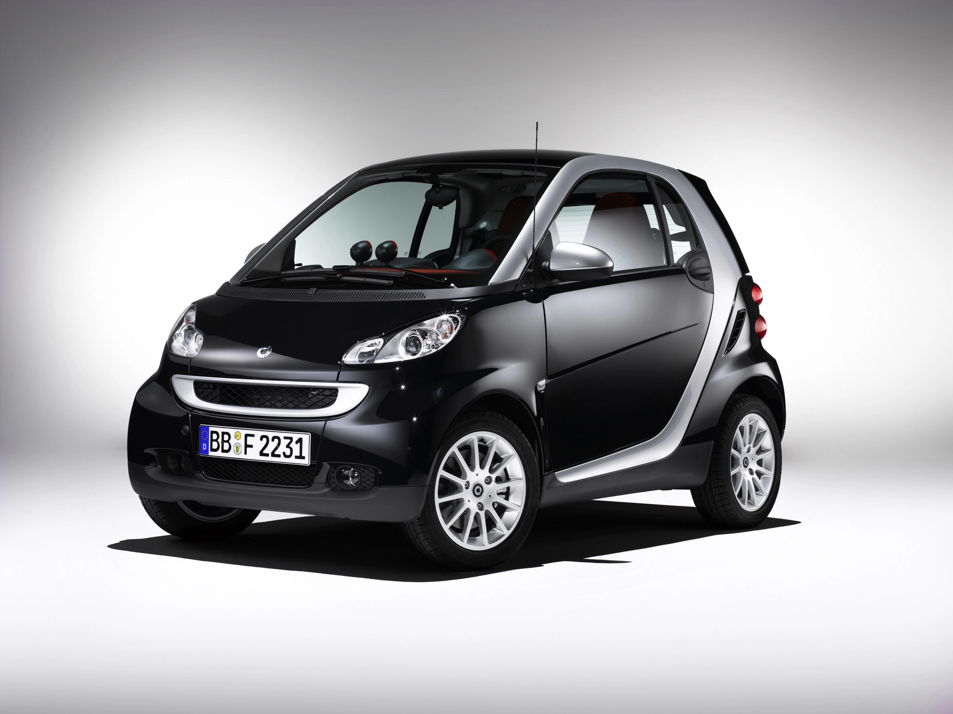 Schwarzer Smart Fortwo vor neutralem Hintergrund, leicht schräg von vorne fotografiert. Fahrzeug steht auf silbernen Alufelgen.