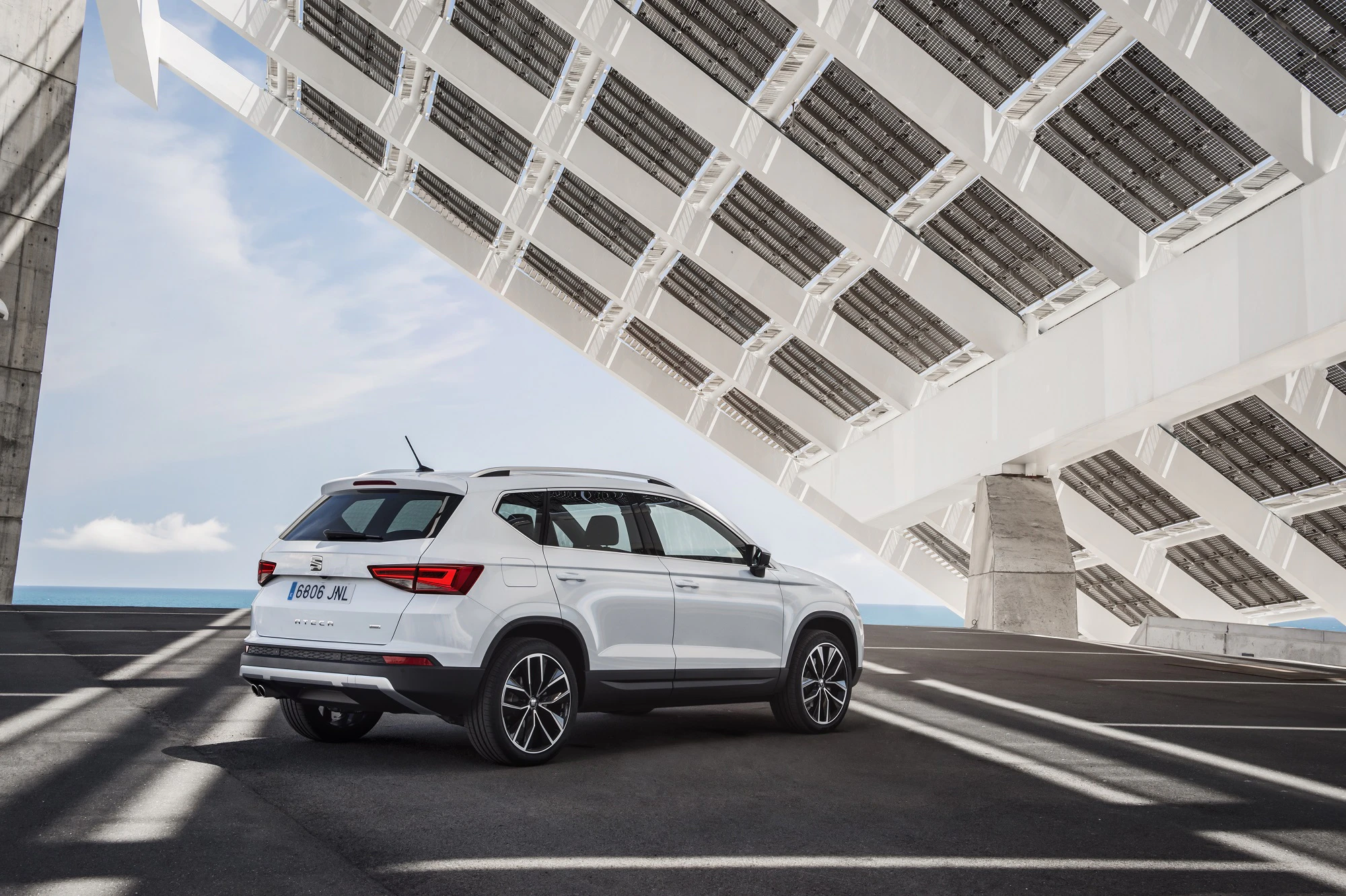 Weißer SUV geparkt unter modernem Architektur-Vordach mit Meer und blauem Himmel im Hintergrund.