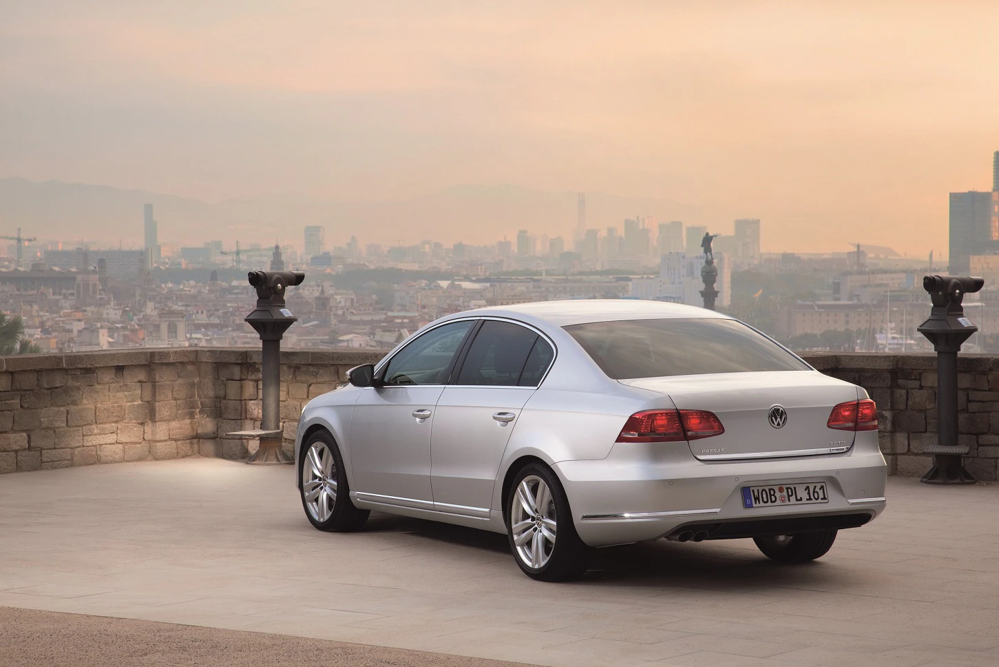 Silberner Volkswagen-Passat steht auf einer Terrasse mit Blick auf eine Stadtlandschaft im Hintergrund unter einem bewölkten Himmel.