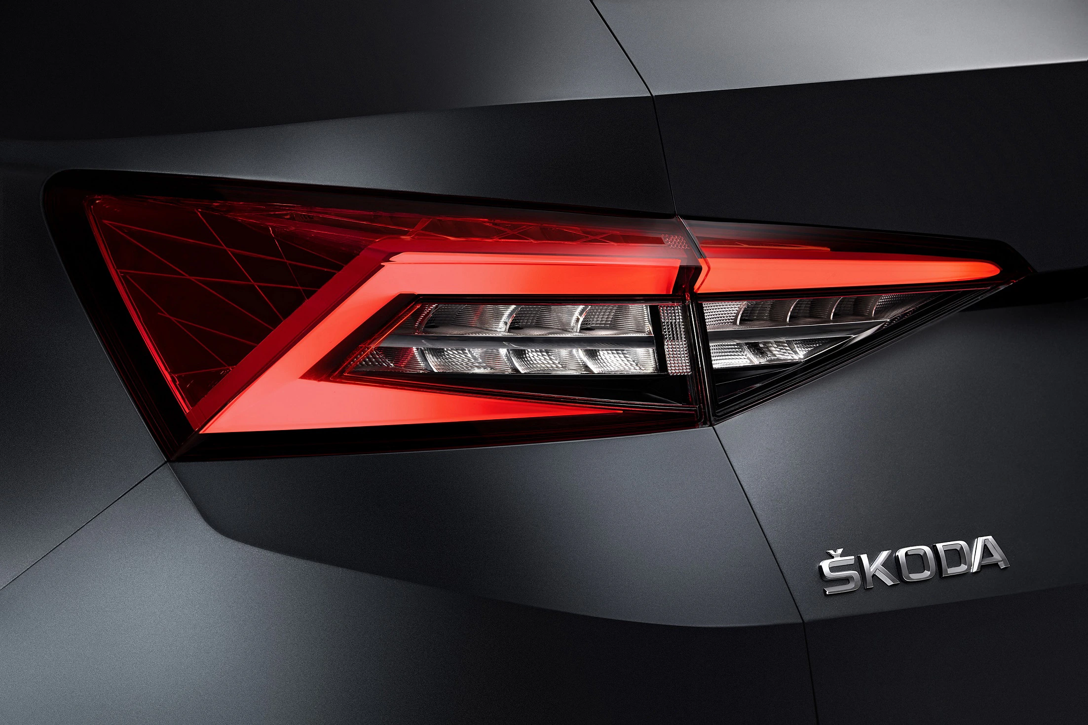 Nahaufnahme eines Škoda-Rücklichts mit markanten, modernen LED-Leuchten und dem Škoda-Logo auf schwarzem Hintergrund.