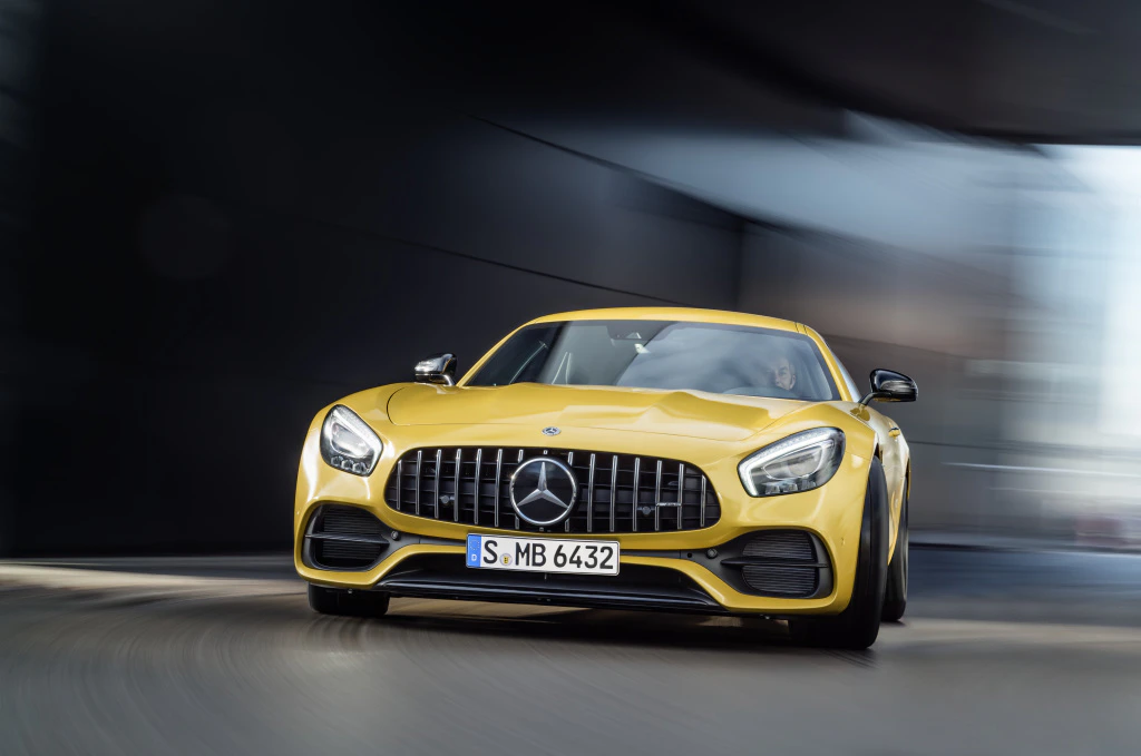 Gelber Mercedes-AMG Sportwagen fährt dynamisch mit verschwommenem Hintergrund, frontal perspektiviert.