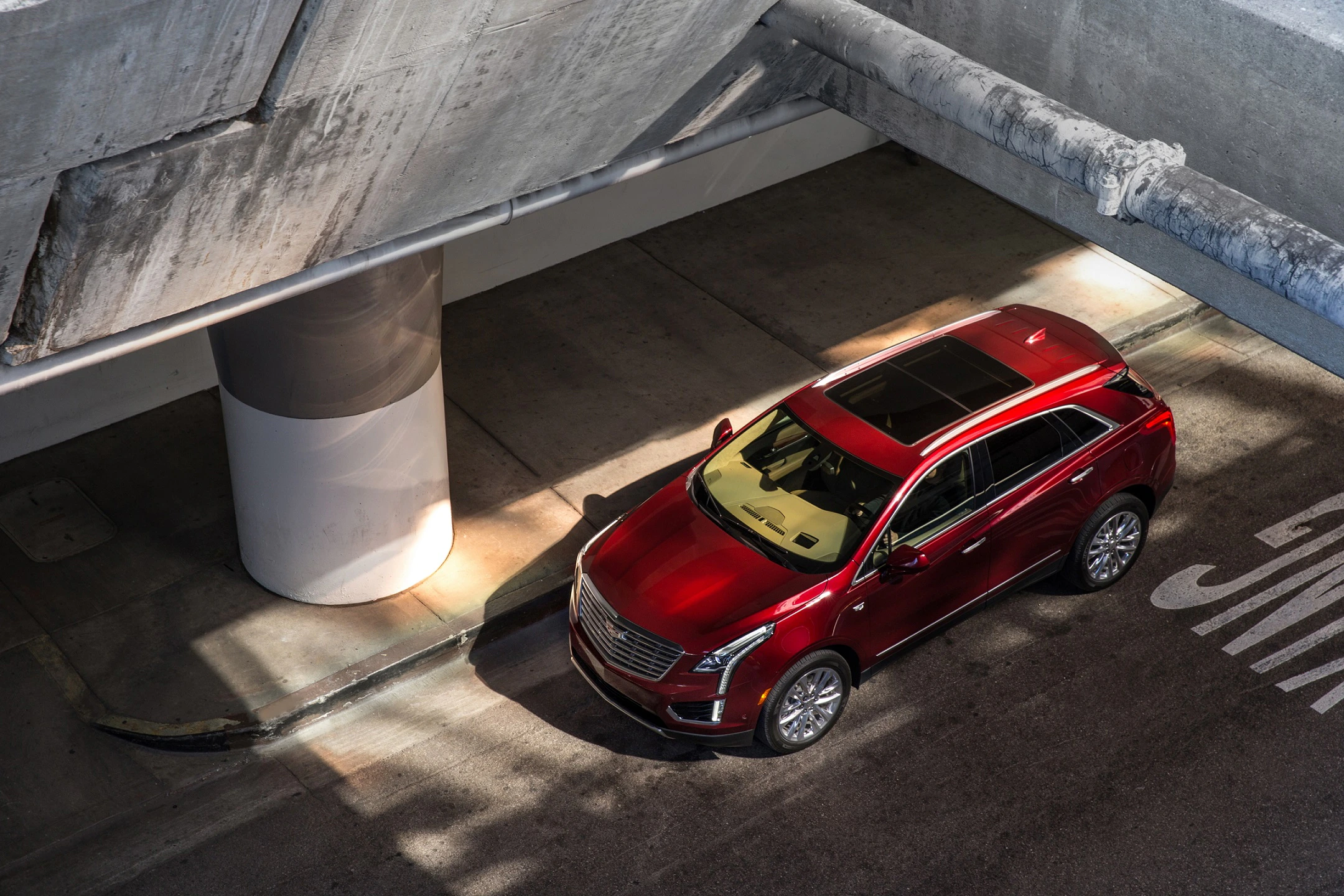 Roter SUV parkt in einem modernen, betonartigen Parkhaus. Sonnenlicht fällt auf das Auto, wodurch es hervorgehoben wird.