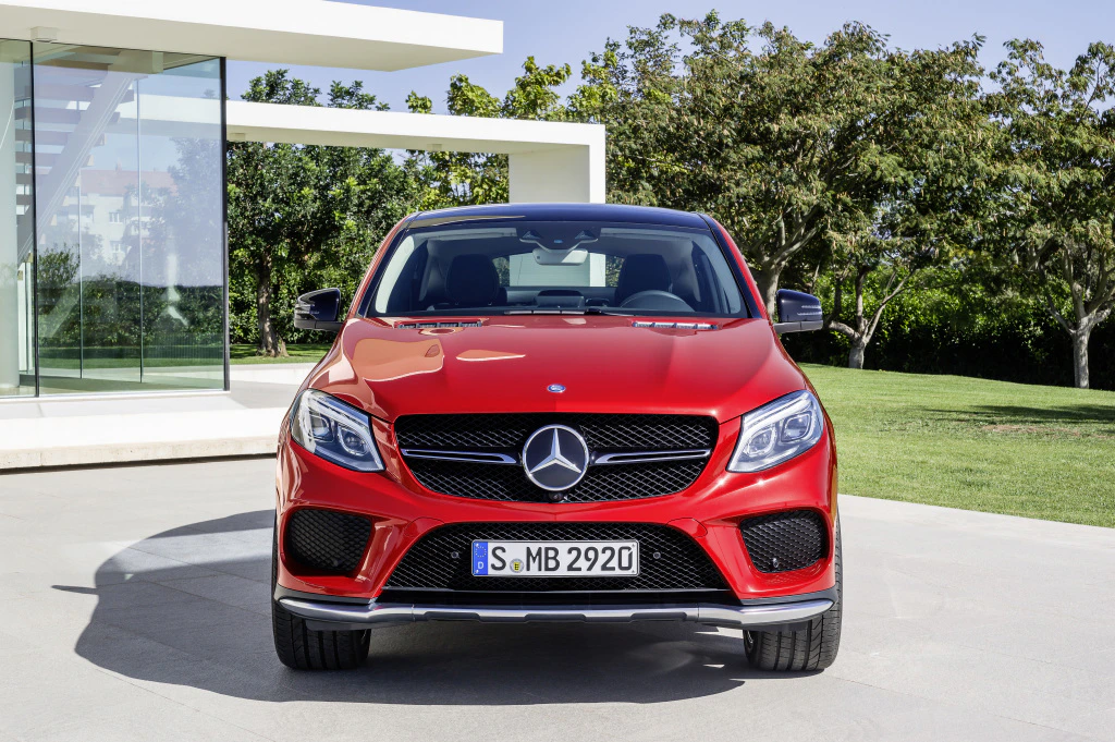 Roter Mercedes-Benz SUV, Frontansicht, auf einer gepflasterten Einfahrt vor einem modernen Gebäude mit Glasfront und Bäumen im Hintergrund.
