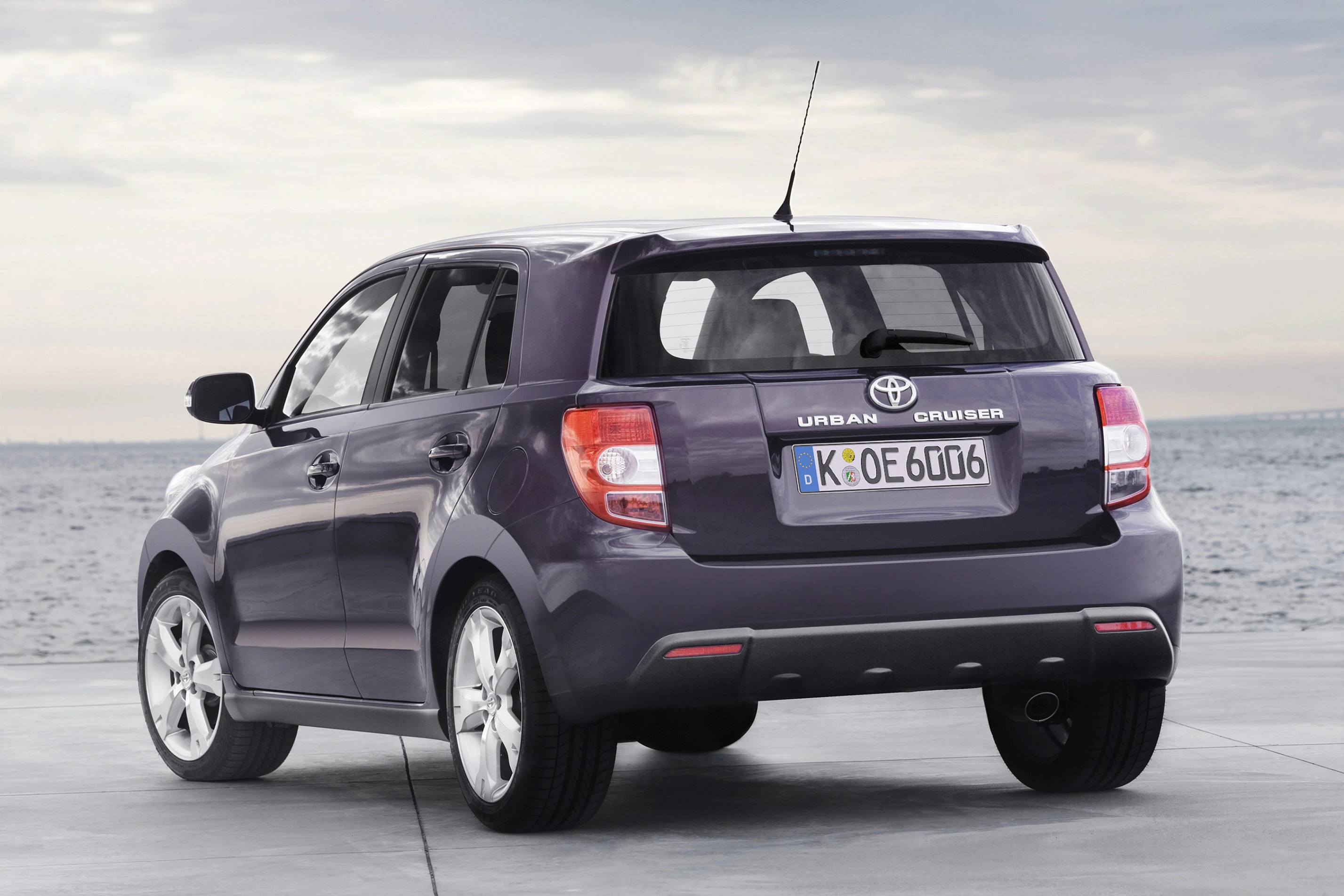 Lila Toyota Urban Cruiser vor bewölktem Himmel und Meer, Seitenansicht von hinten. Fahrzeug hat ein deutsches Kennzeichen.