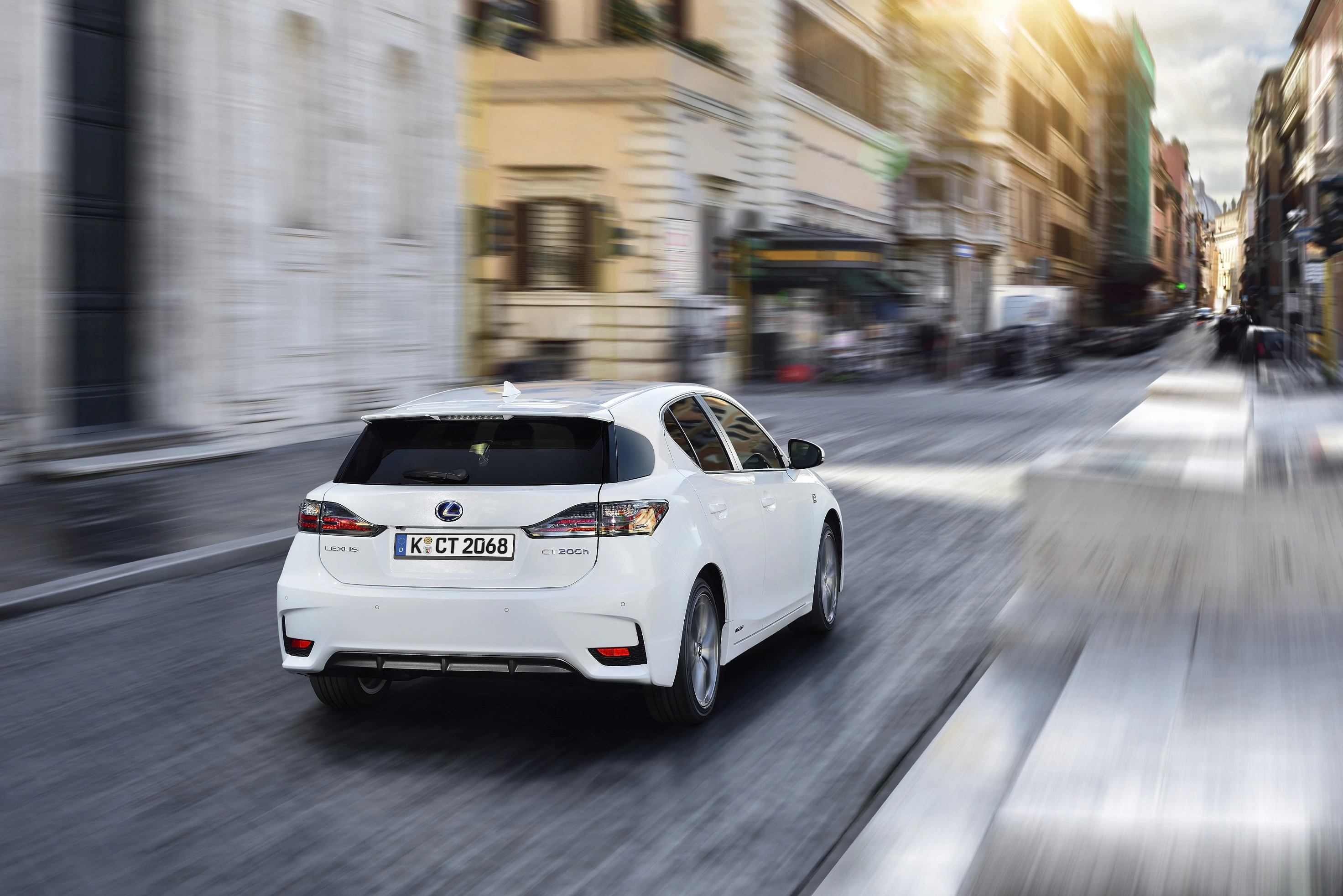 Weißer Lexus fährt schnell durch eine belebte Stadtstraße mit historischen Gebäuden im Hintergrund.
