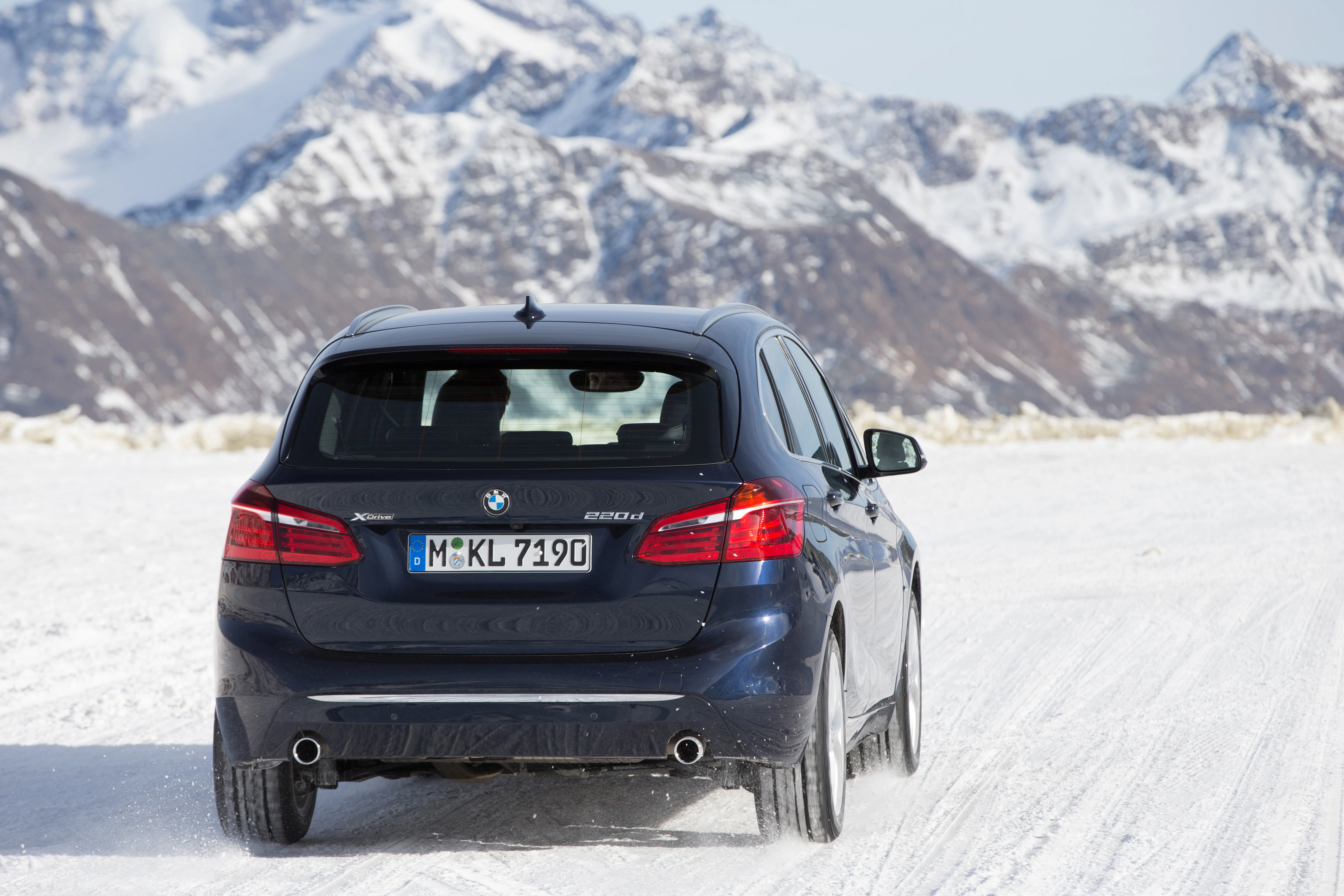 BMW X5 fährt auf schneebedeckter Straße in bergiger Landschaft. Schneeberge im Hintergrund bei klarer Sicht.