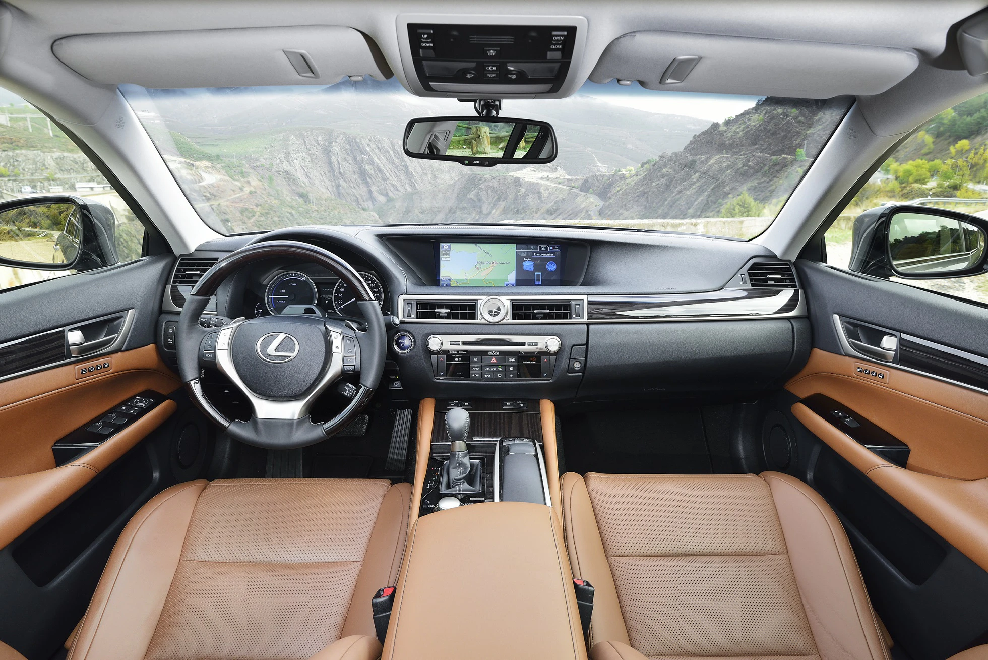 Innenraum eines Autos mit braunen Ledersitzen, modernem Lenkrad und einem großen Display in der Mittelkonsole, umgeben von Berglandschaft.