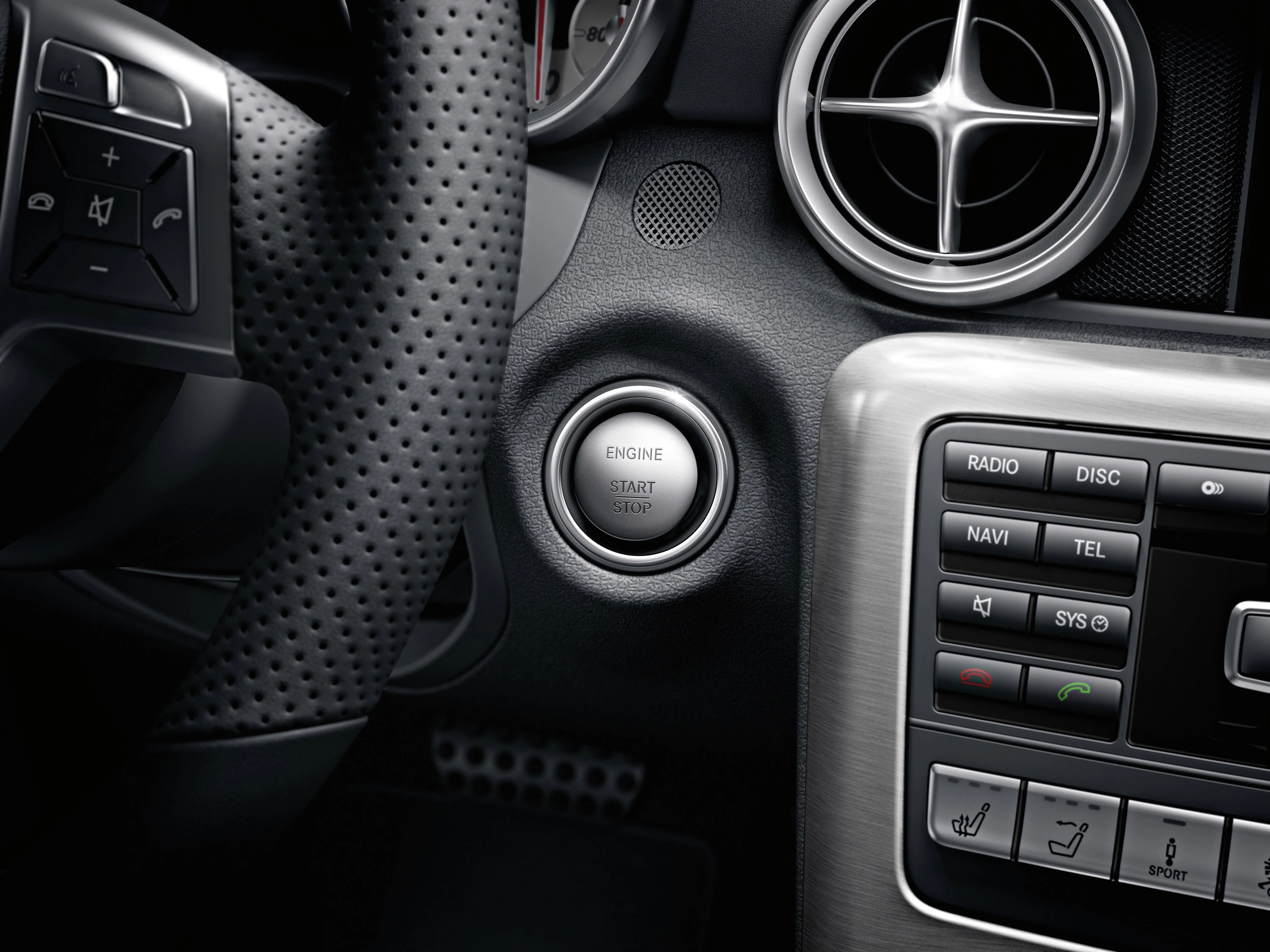 Nahaufnahme eines Autos mit Startknopf, Lüftungsschlitz und Lenkrad. Knöpfe für Radio und Navigation sind sichtbar.