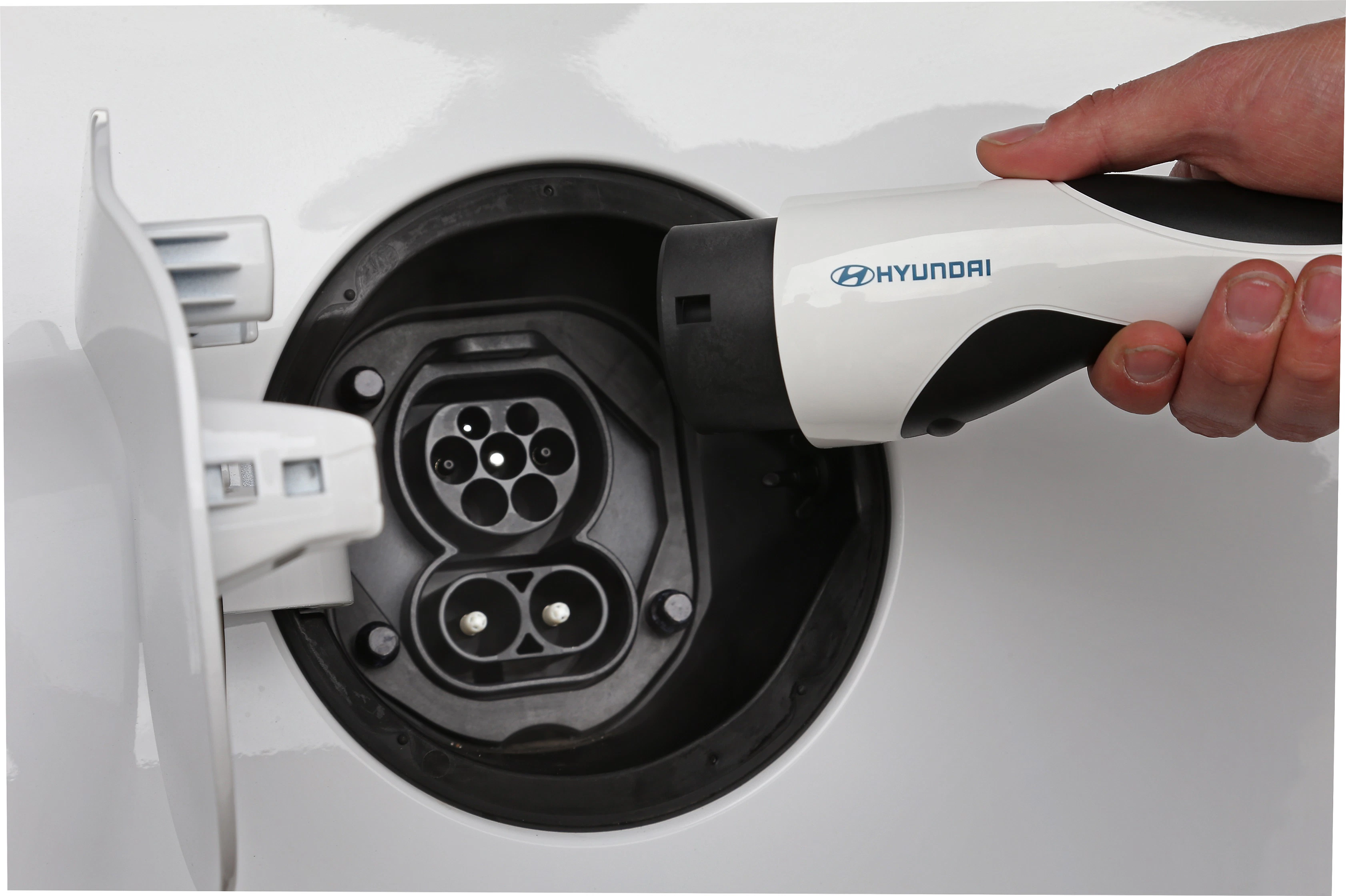 Nahaufnahme eines Elektrofahrzeugs, das an eine Ladestation angeschlossen wird. Eine Hand hält den Ladeanschluss mit Hyundai-Logo.