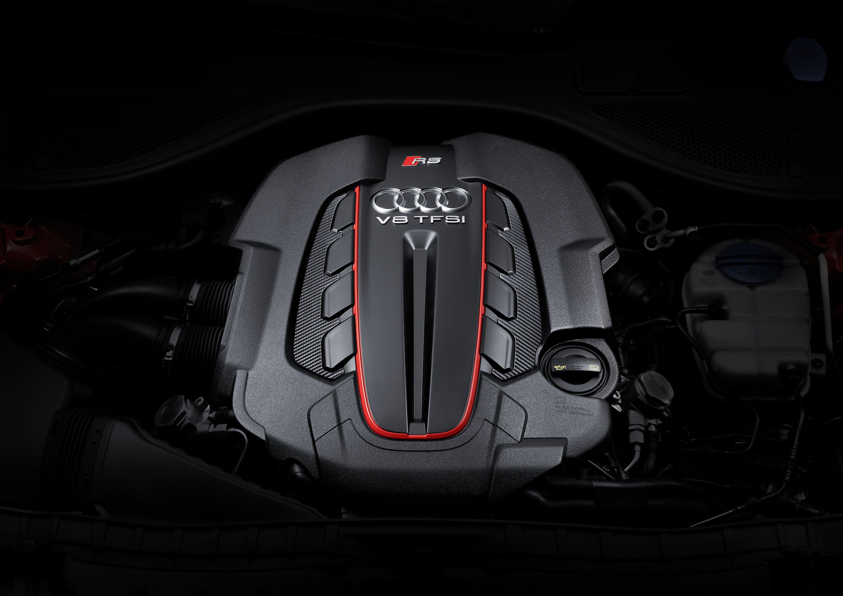 Nahaufnahme eines V8 TFSI Motors mit Audi-Logo, schwarzes Gehäuse und roten Details, beleuchtet vor dunklem Hintergrund.