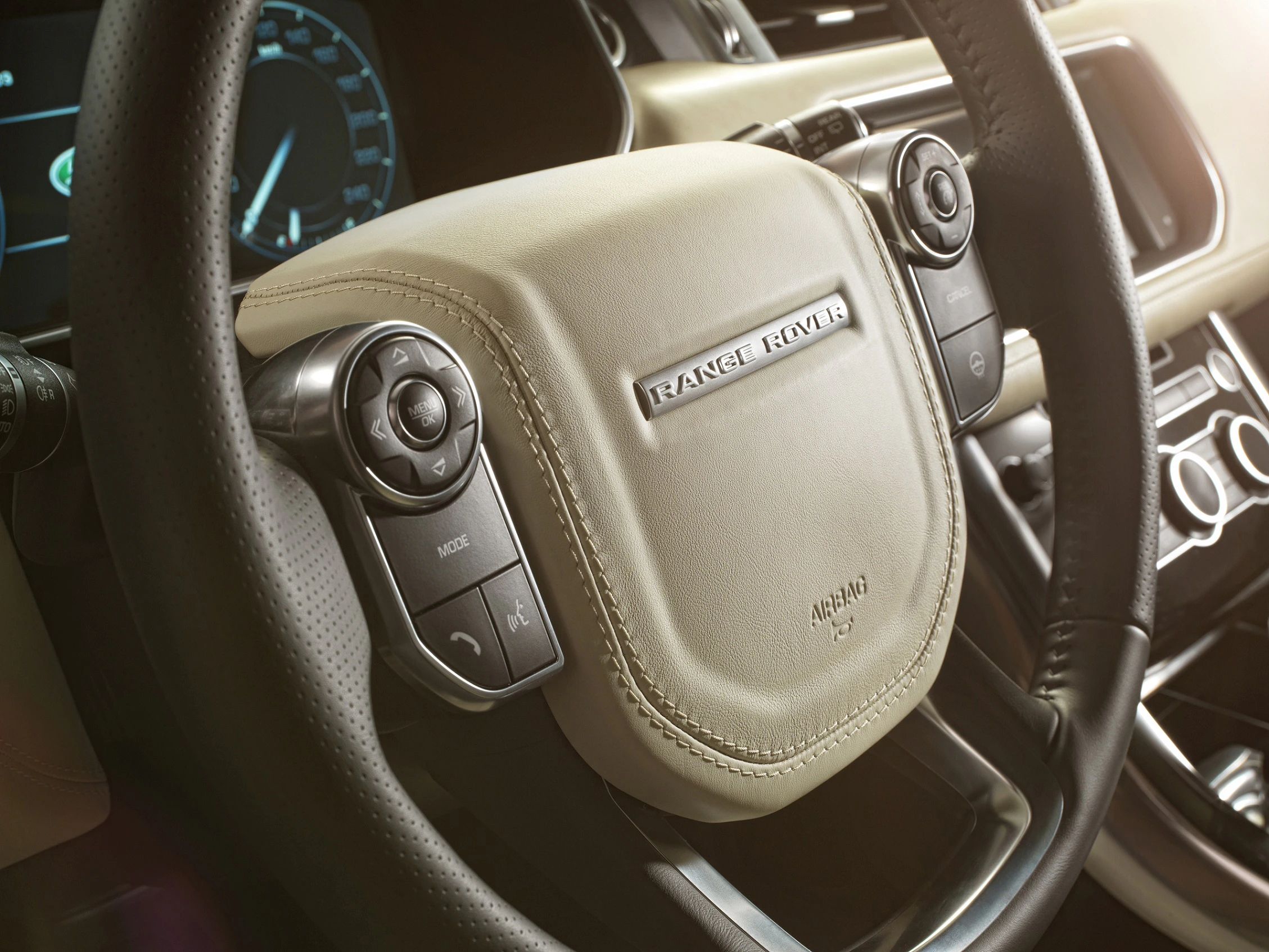 Lenkrad eines Range Rover mit beige-brauner Lederverkleidung und Multifunktionstasten, Armaturenbrett im Hintergrund.
