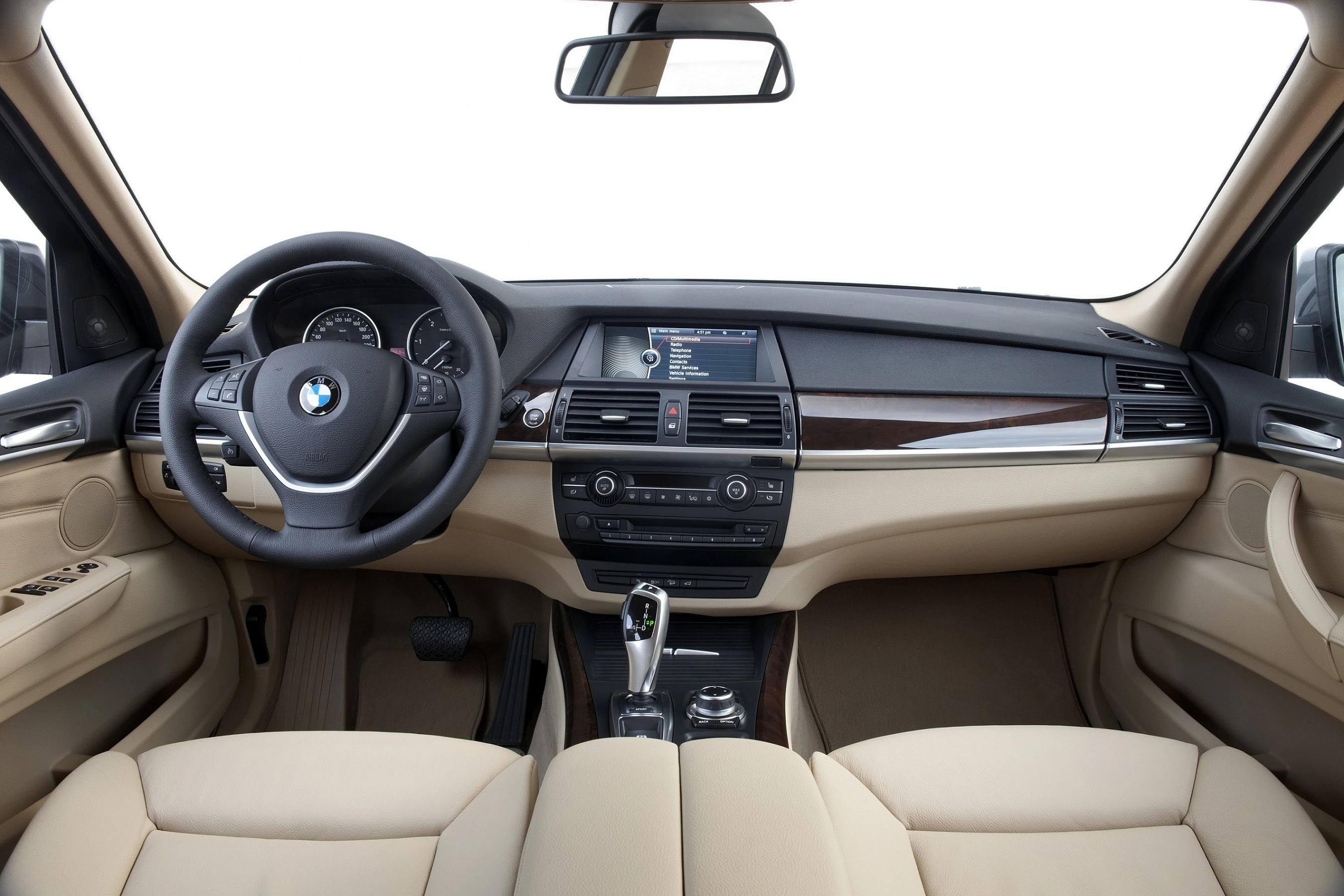 Innenraum eines Autos mit beigem Leder, BMW-Lenkrad, Mittelkonsole mit digitalen Anzeigen und Holzverkleidung, helle Umgebung.