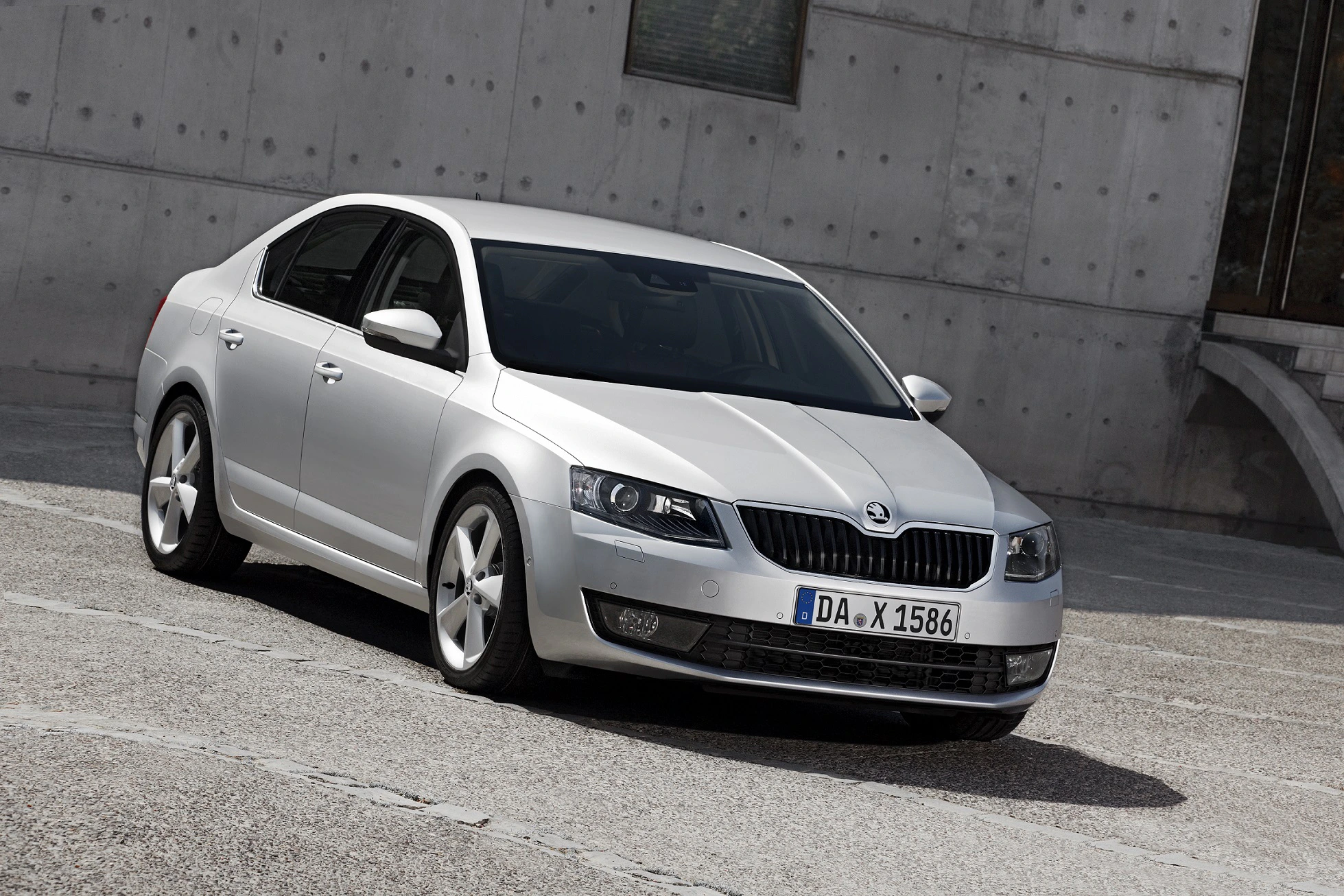 Silberner Škoda Octavia Limousine, geparkt vor einer grauen Betonwand, Frontansicht.