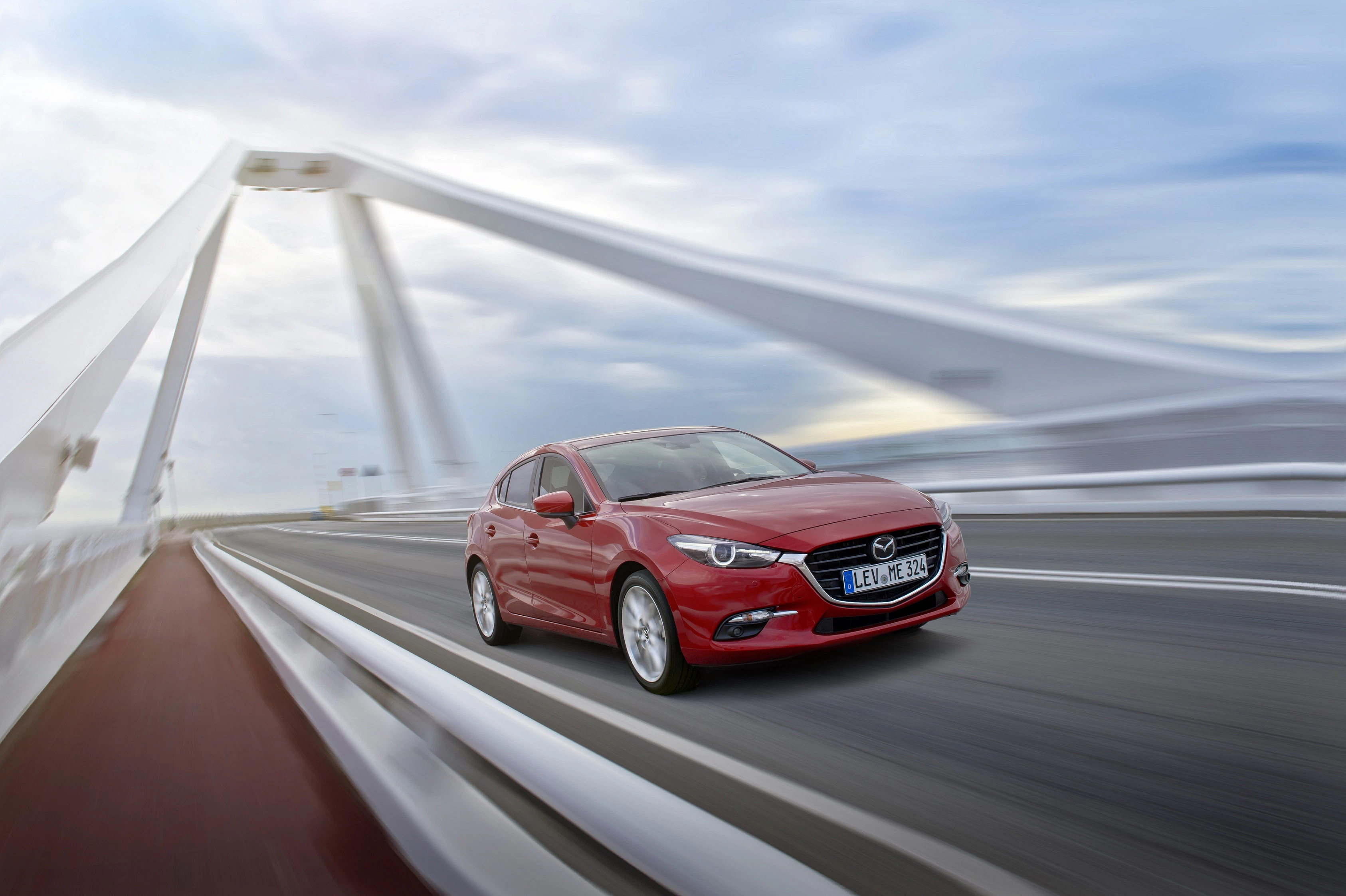 Rotes Auto fährt über moderne weiße Brücke bei bewölktem Himmel, Perspektive von vorn links.