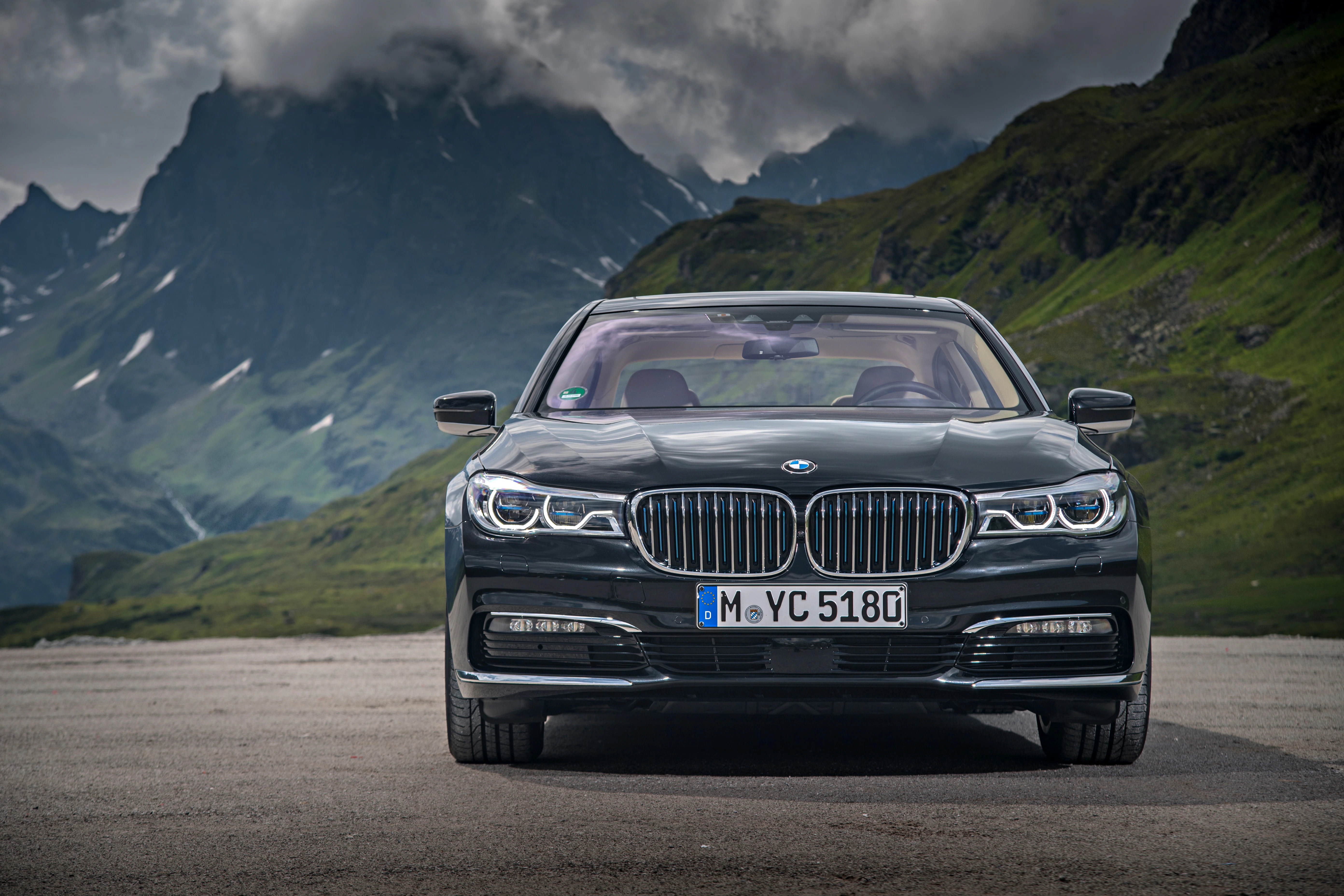 Luxuriöser, schwarzer BMW auf einer Bergstraßenkulisse, umgeben von grünen Hügeln und bewölkten, felsigen Gipfeln im Hintergrund.