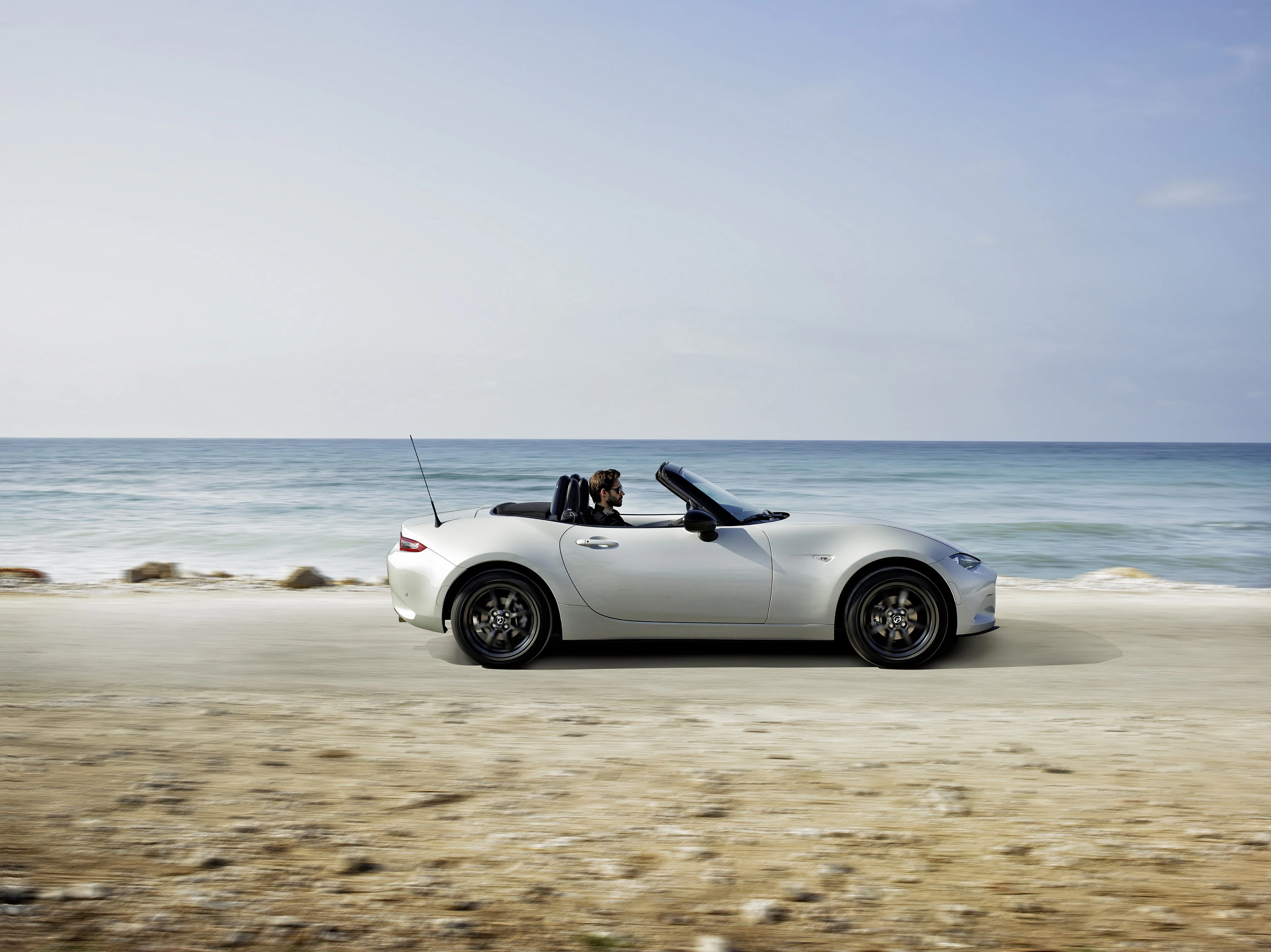 Ein weißes Cabrio fährt am Meer entlang. Der Himmel ist klar, und die Fahrerin trägt Sonnenbrille.