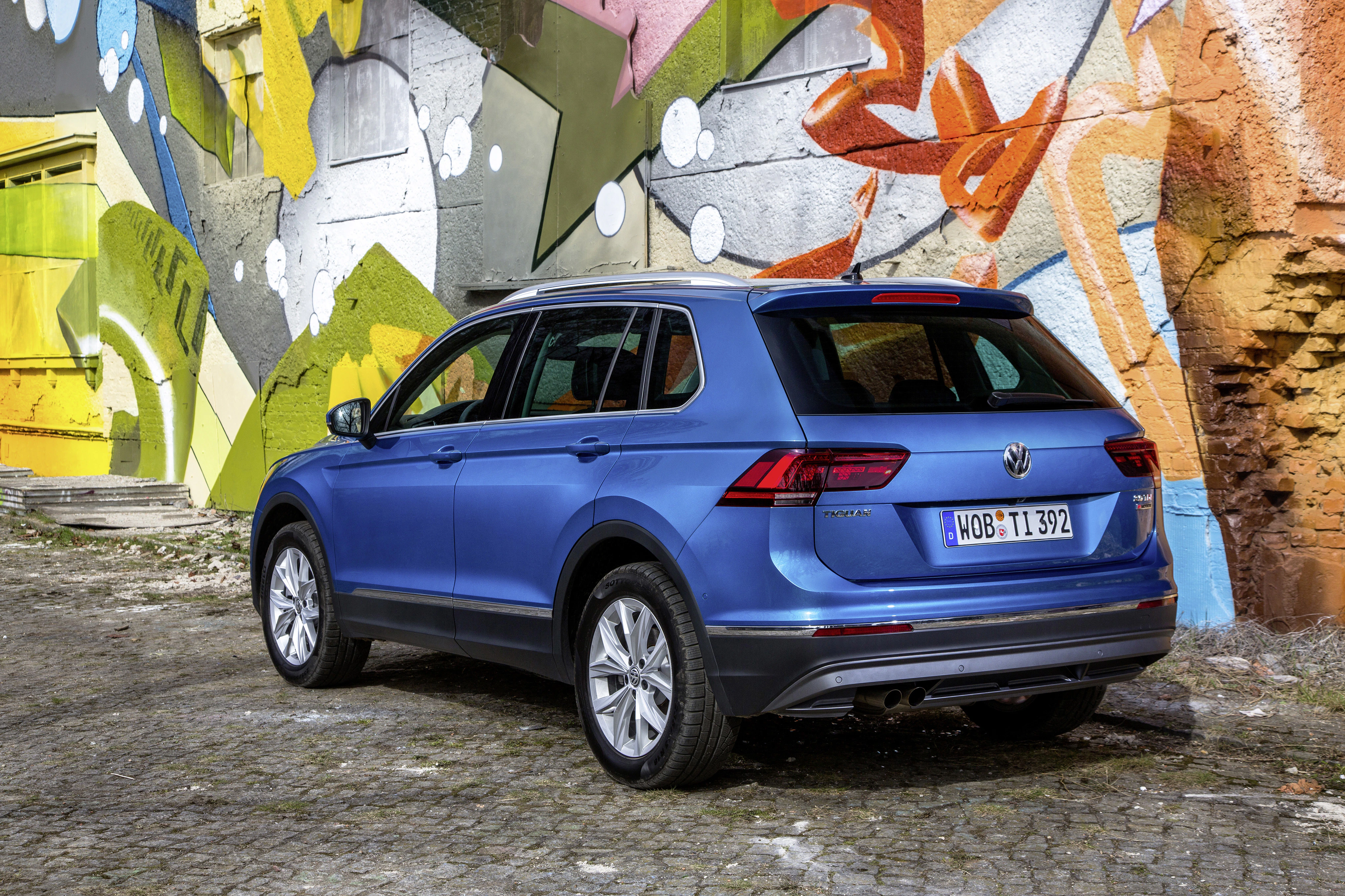 Blauer SUV vor einer farbenfrohen Graffiti-Wand, geparkt auf einem Pflastersteinboden.