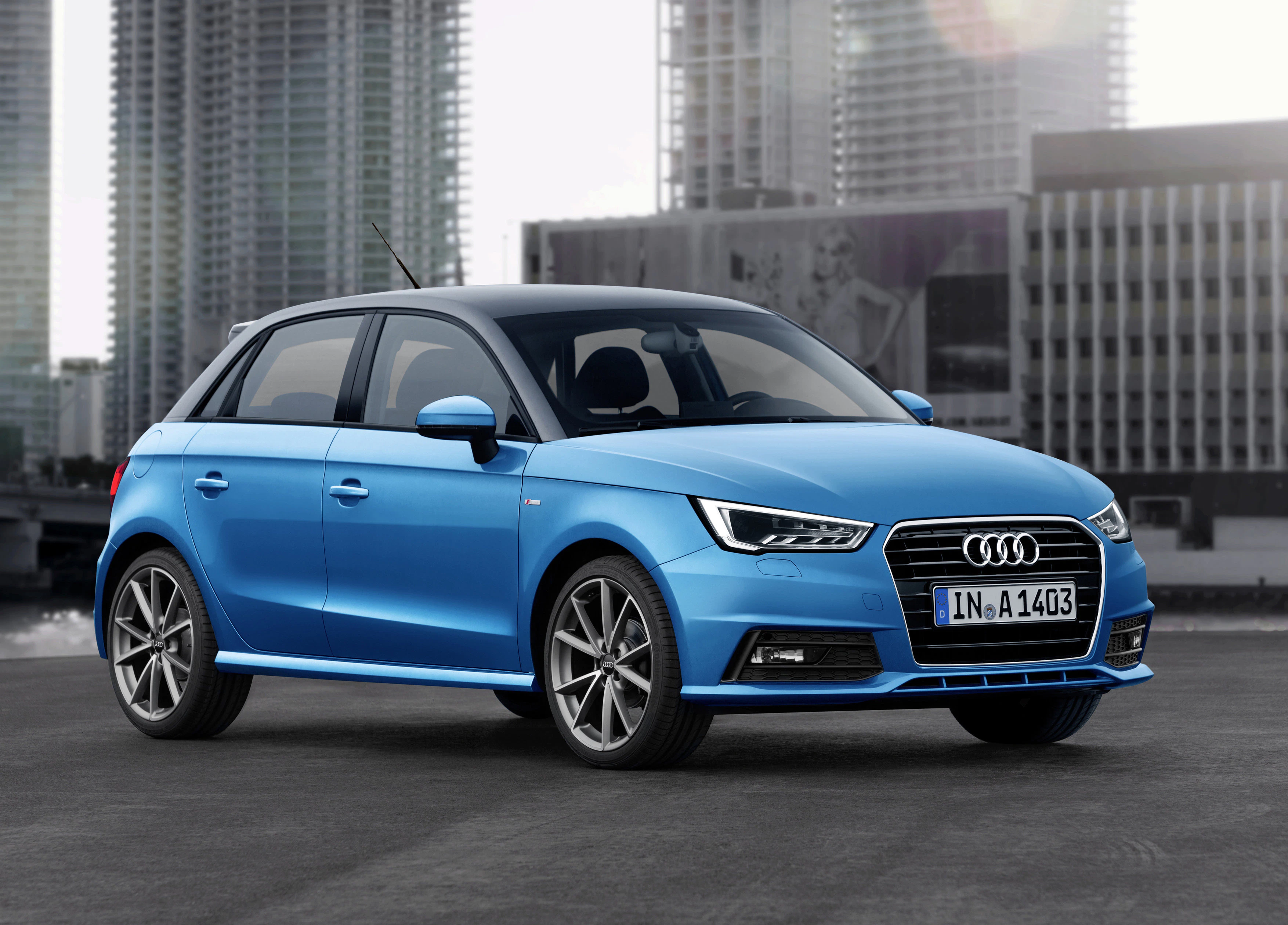 Blauer Audi A1 Sportback steht auf einem städtischen Parkplatz vor modernen Hochhäusern bei Tageslicht.