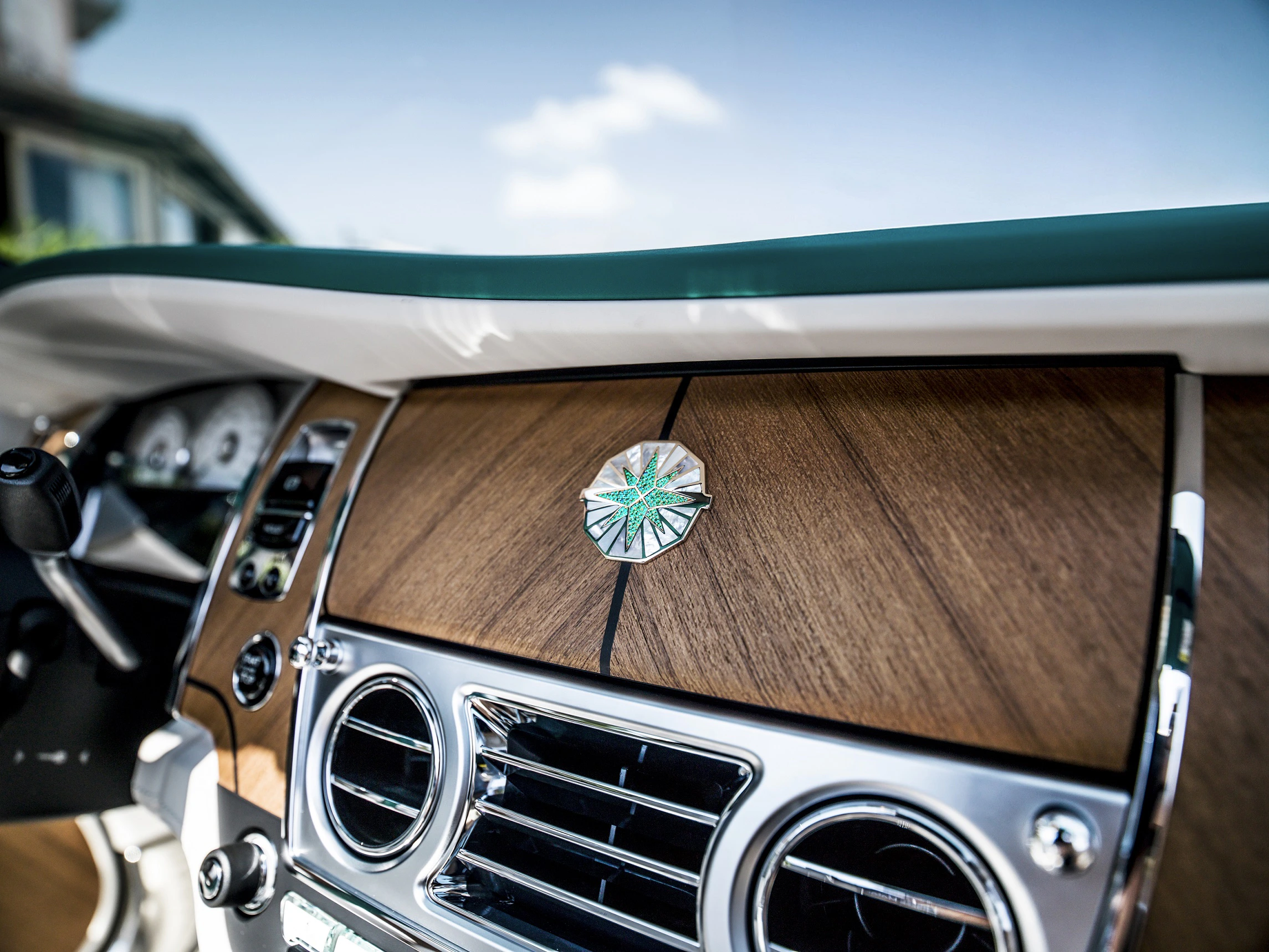 Luxuriöses Autointerieur mit hölzernem Armaturenbrett, verchromten Lüftungsschlitzen und markantem Emblem in der Mitte.