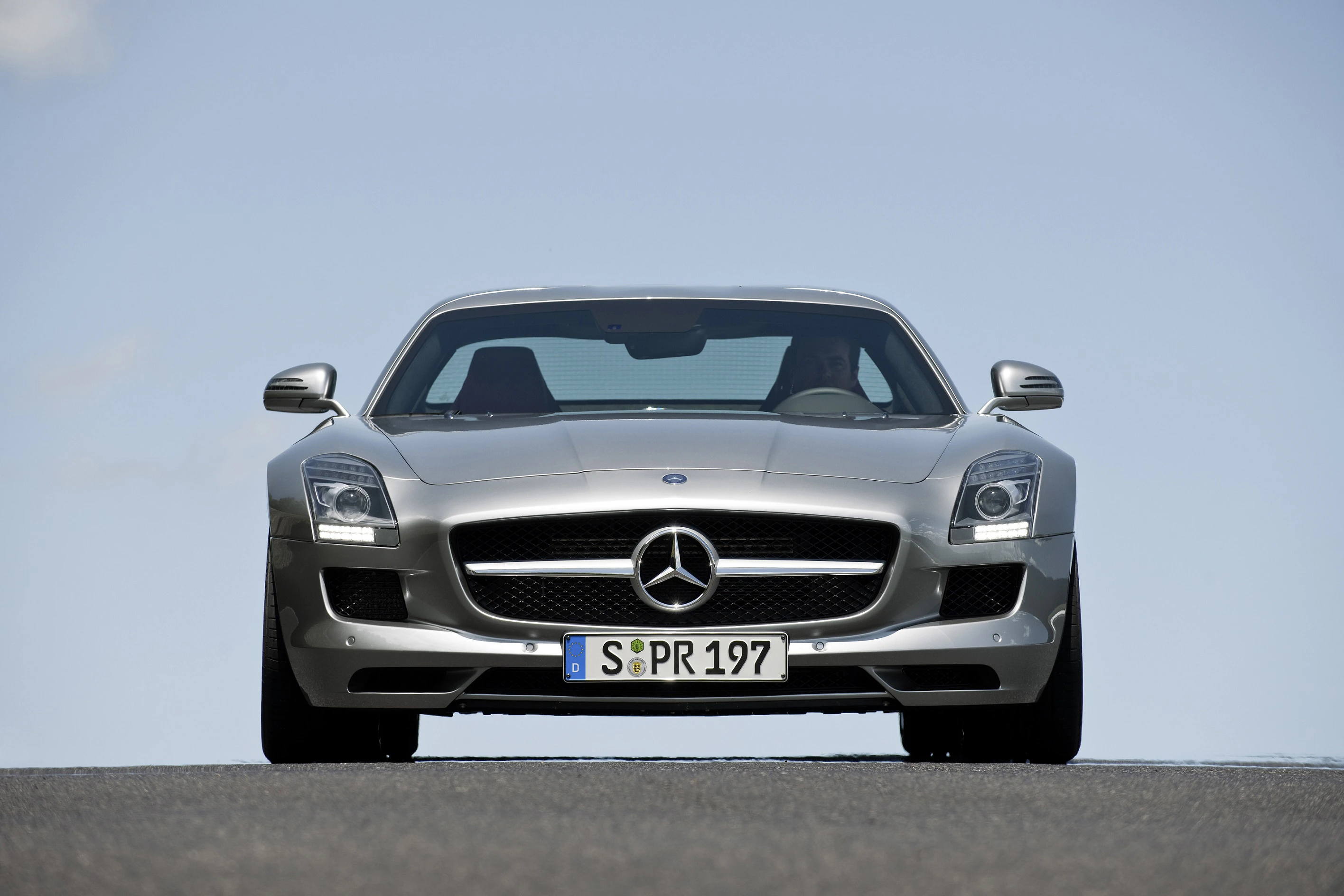 Silberner Mercedes-Benz SLS AMG, Frontansicht auf offener Straße bei klarem Himmel.