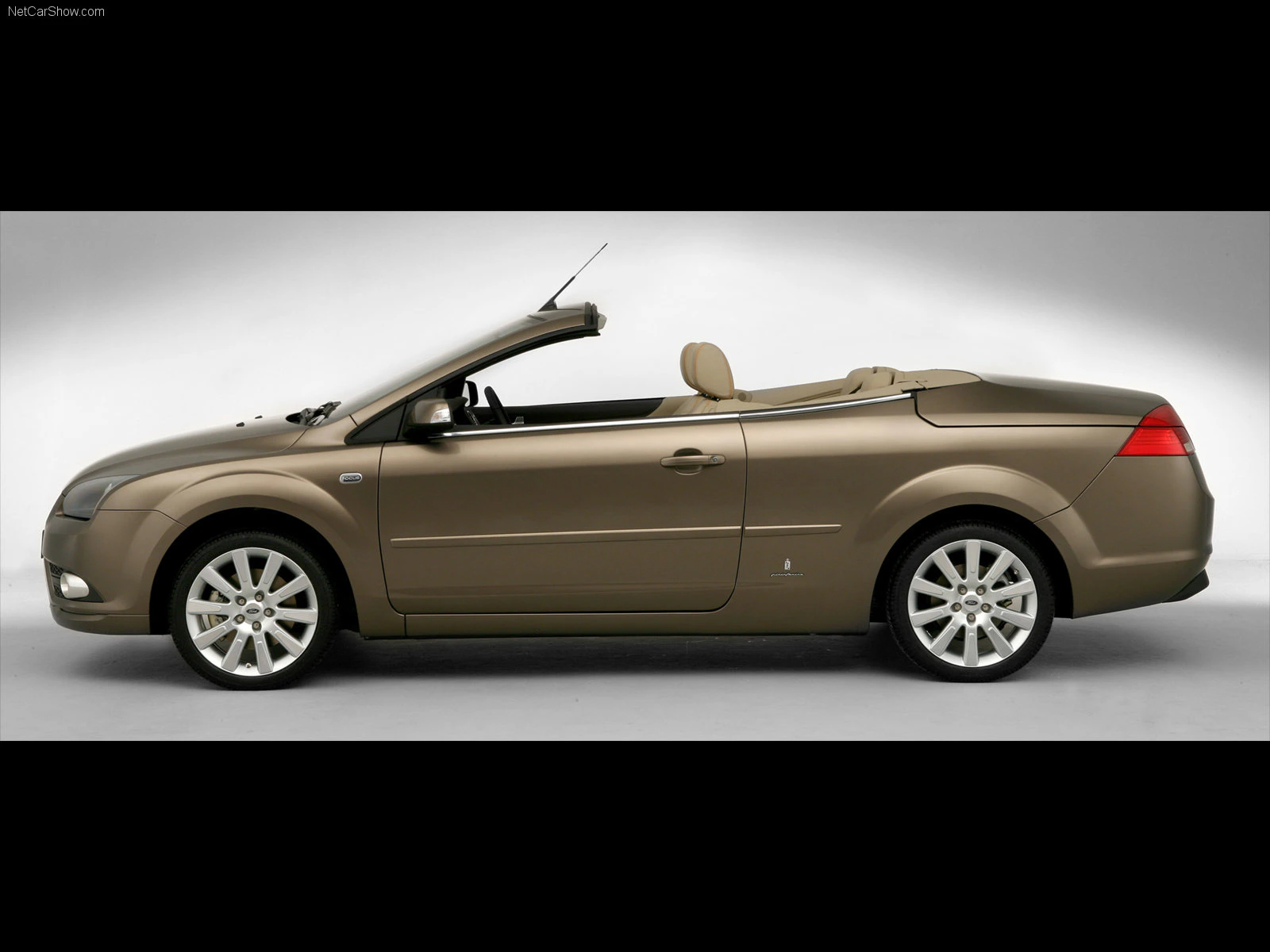 Braunes Cabriolet-Auto mit geöffnetem Verdeck, seitliche Ansicht. Heller Innenraum, modernes Design, silberne Felgen auf weißem Hintergrund.