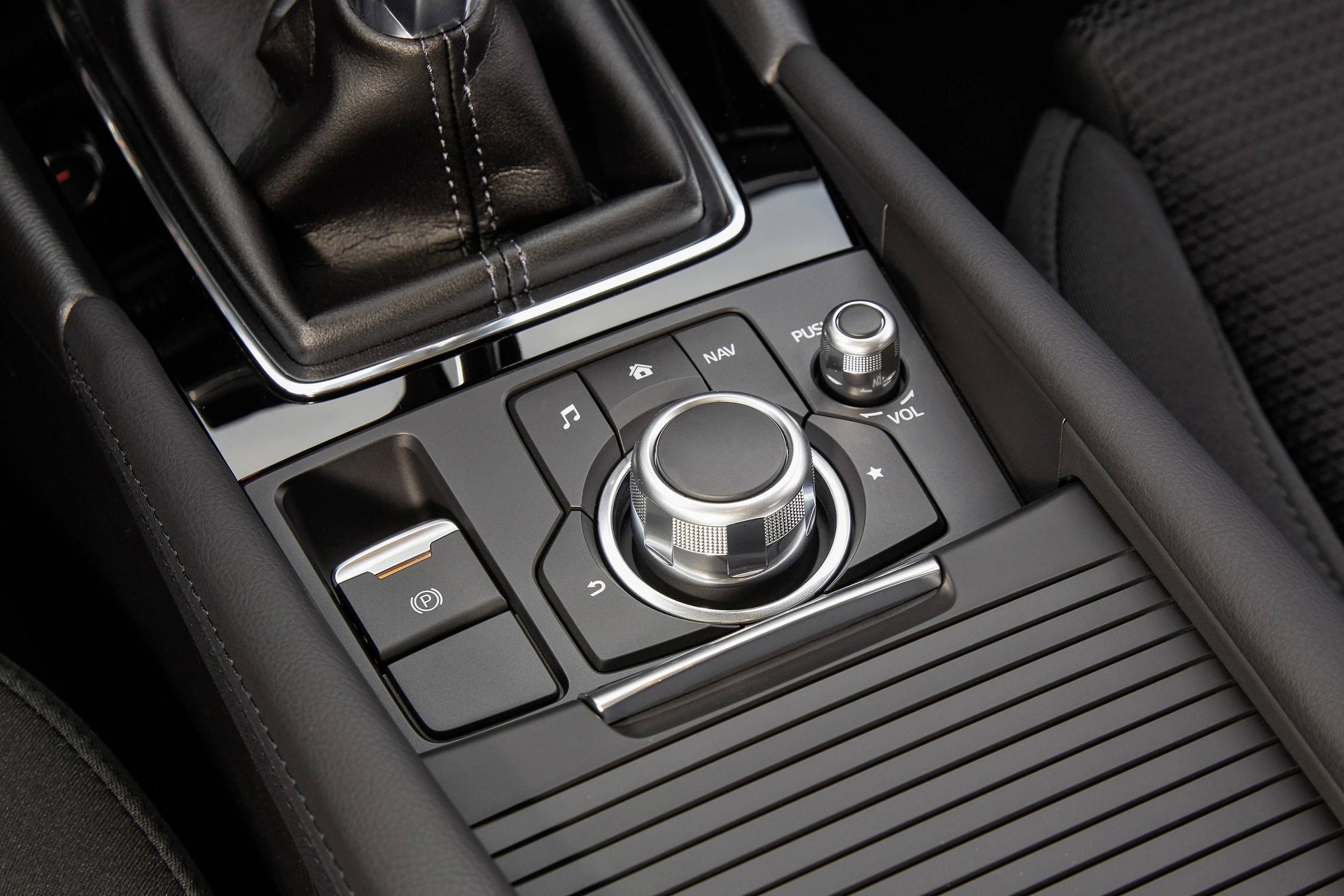 Autokonsolen-Bedienfeld mit Drehregler, Musik- und Navigationstasten, Lederverkleidung, zwischen den Vordersitzen eines Fahrzeugs.