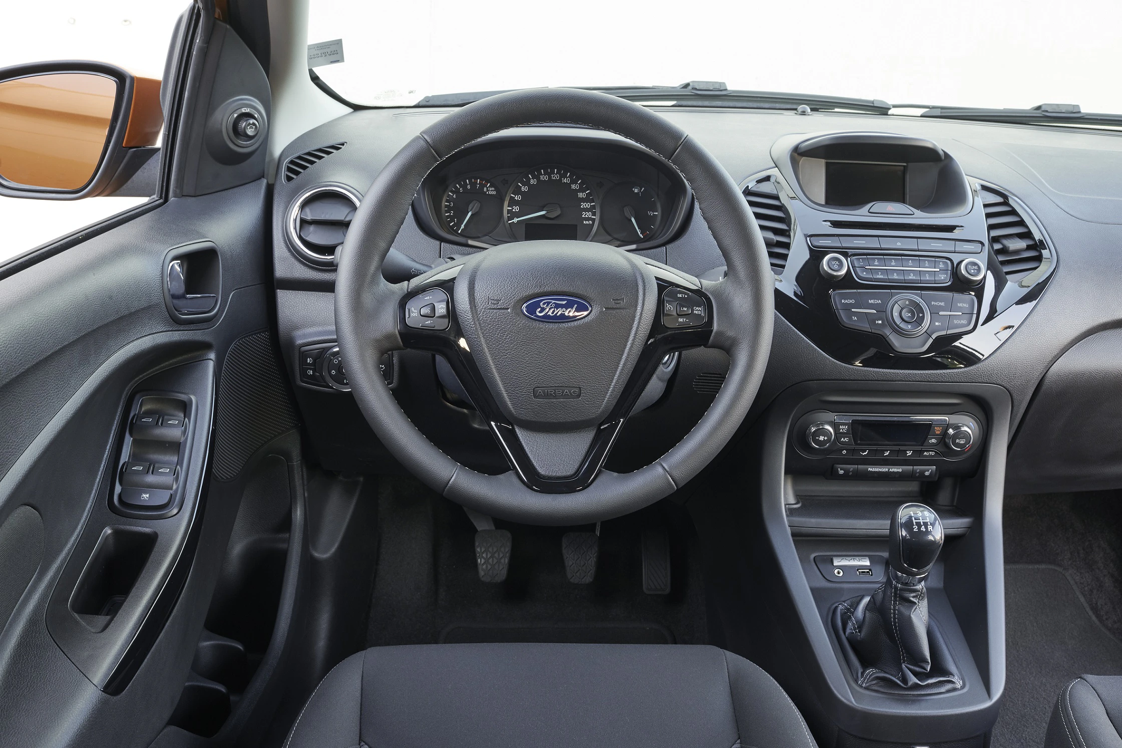 Innenraum eines Autos mit Ford-Logo auf dem Lenkrad, Schalthebel in der Mittelkonsole, Armaturenbrett mit Instrumenten und Radiobedienelementen.