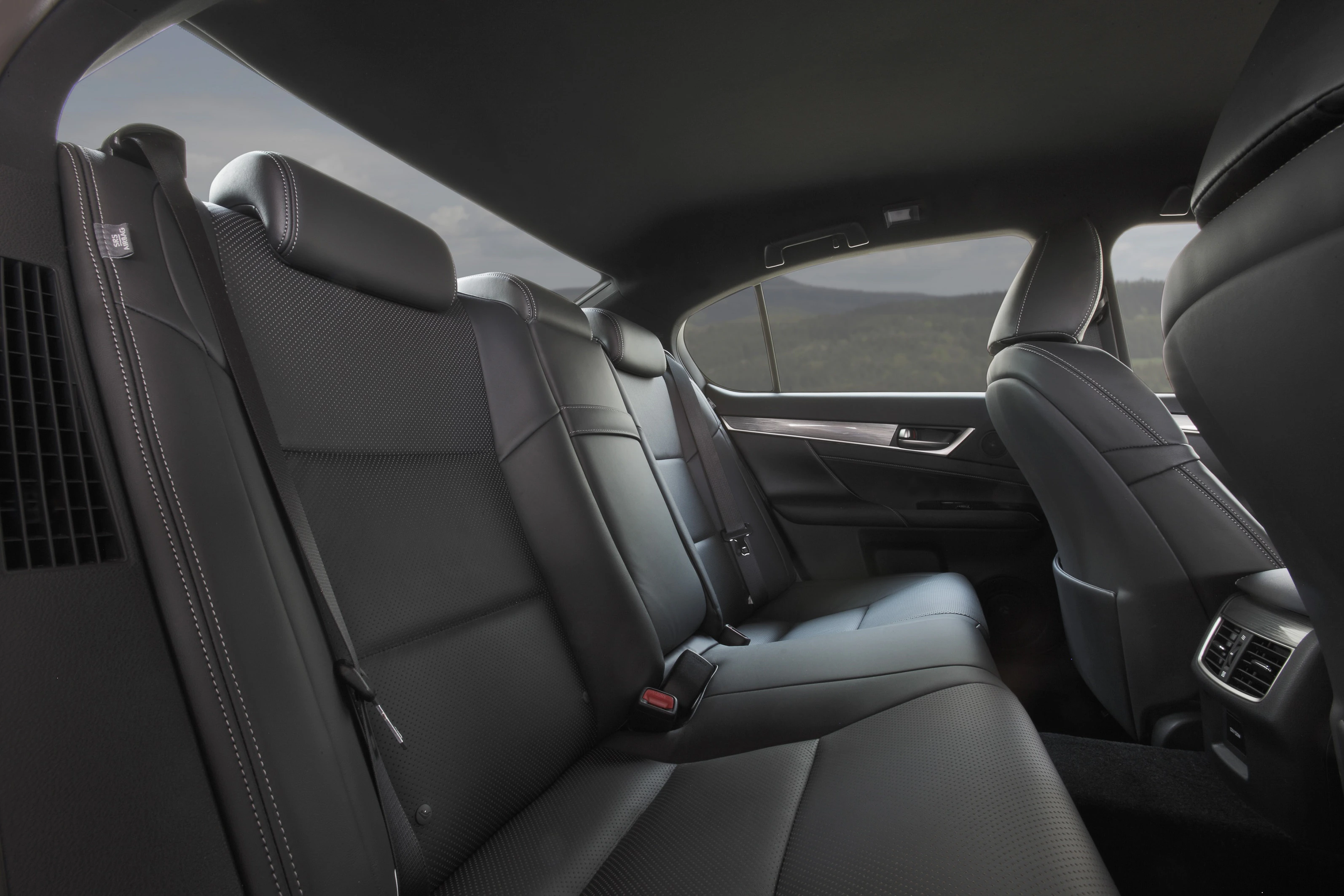 Schwarzer Ledersitz eines luxuriösen Autos, geräumig, mit stilvollen Nähten und grauem Himmel durch die Fenster im Hintergrund sichtbar.