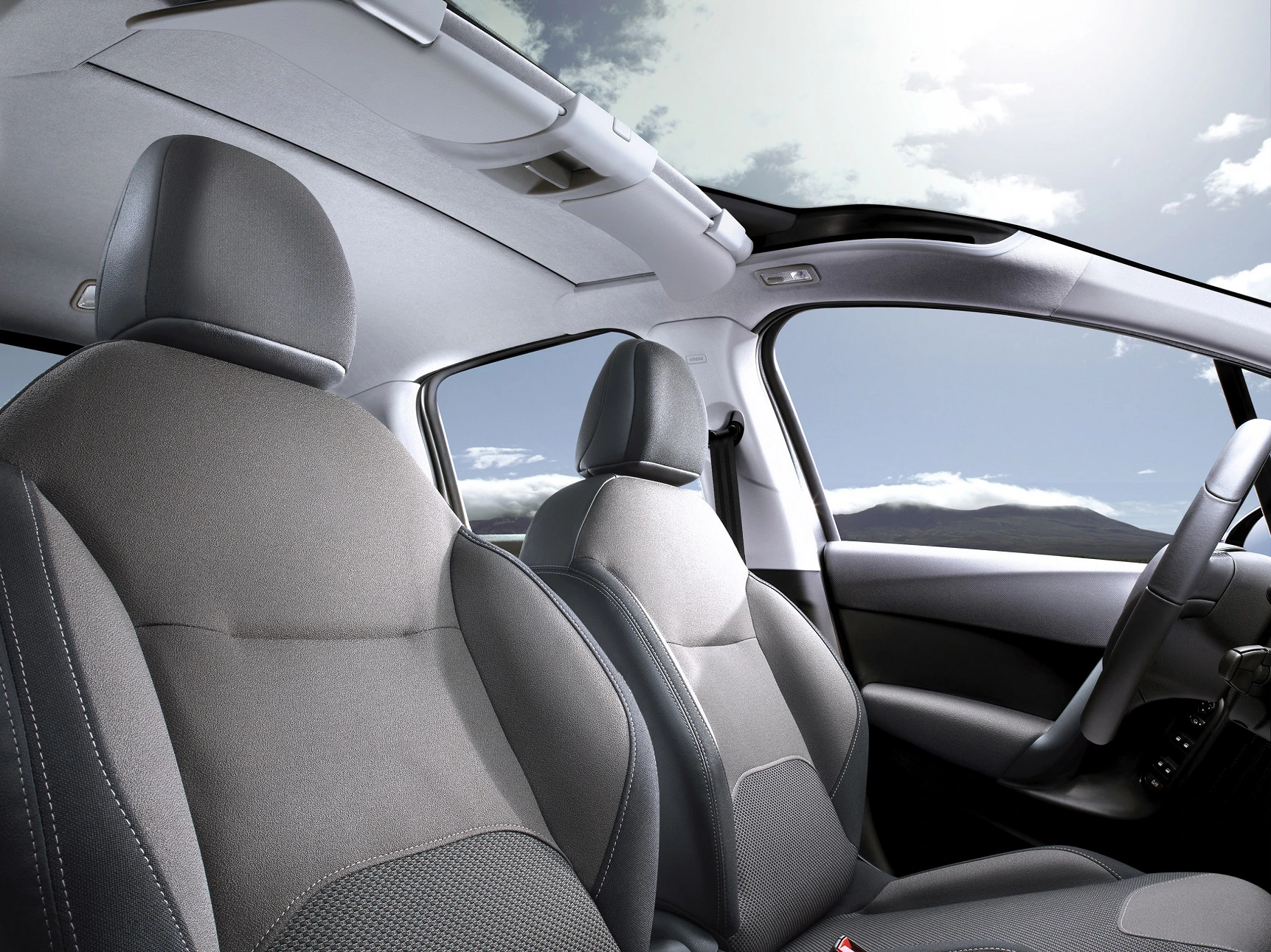 Innenraum eines Autos mit Panoramadach und grauen Polstersitzen. Himmel mit einigen Wolken ist durch das Dach sichtbar.