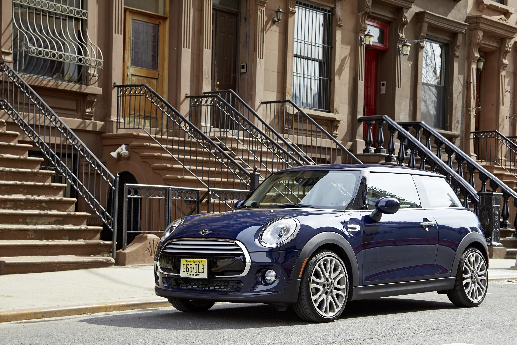 Blauer Mini Cooper parkt vor einer Reihe von braunen Stadthäusern mit Treppen in einer urbanen Umgebung bei Tageslicht.