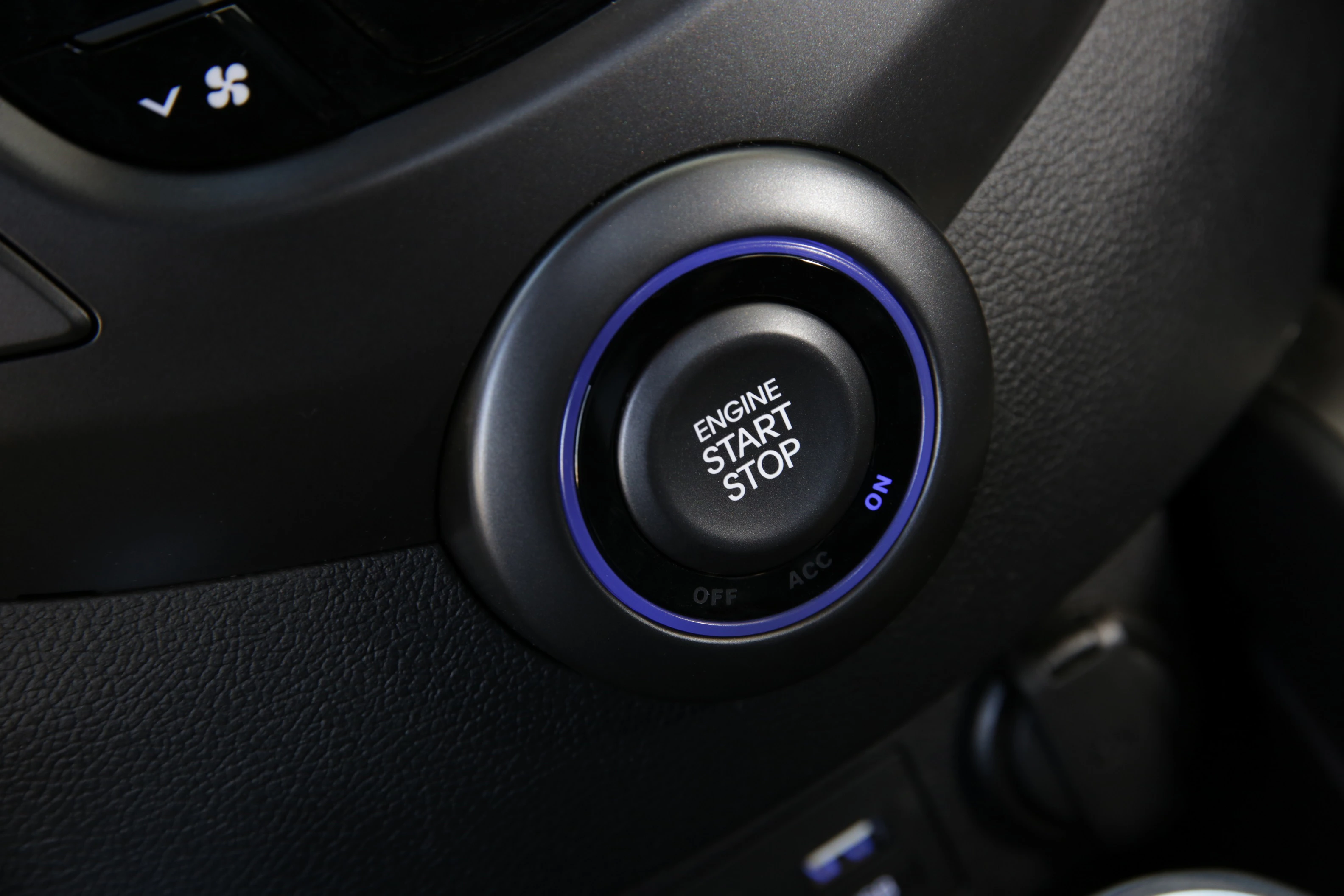Nahaufnahme eines modernen Auto-Startknopfes mit der Aufschrift "Engine Start Stop" in einem Fahrzeuginterieur.