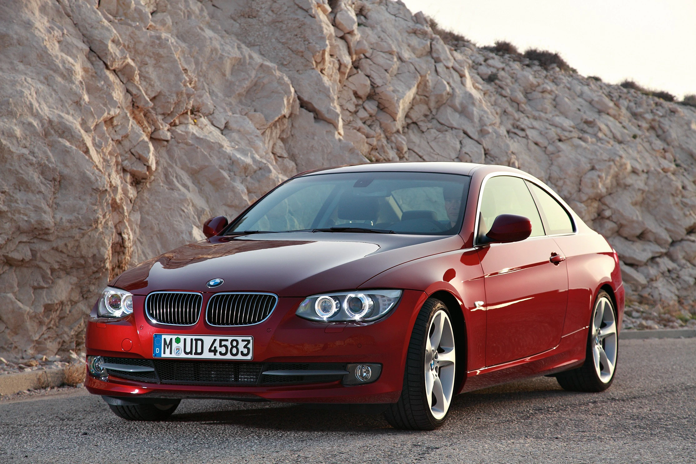Roter BMW-Coupé auf einer Straße vor einer felsigen Landschaft bei Sonnenuntergang.